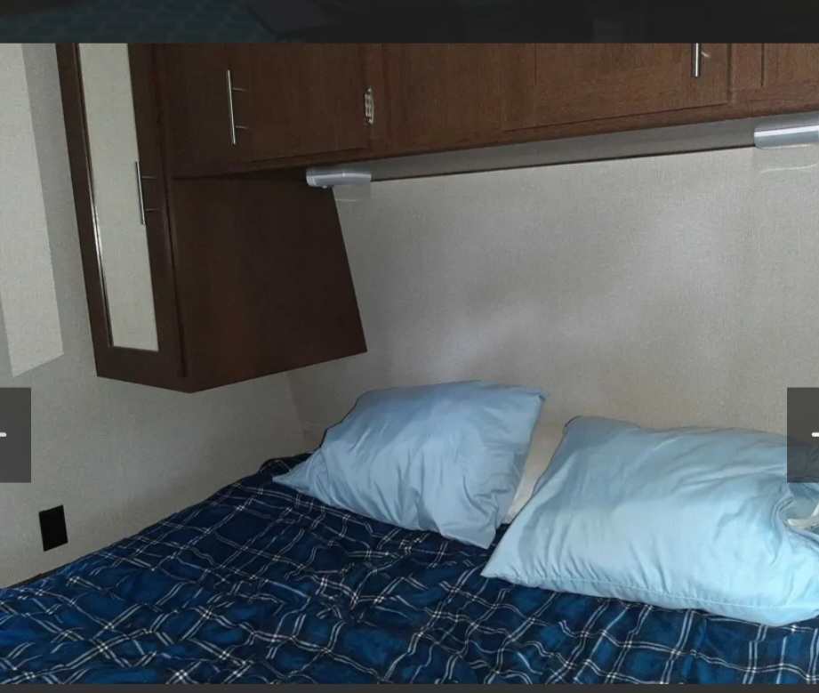 RV rental's cozy bedroom: bed with blue plaid comforter & pillows, overhead cabinets. Ideal for a comfortable sleep.. Avenger ATI 2019