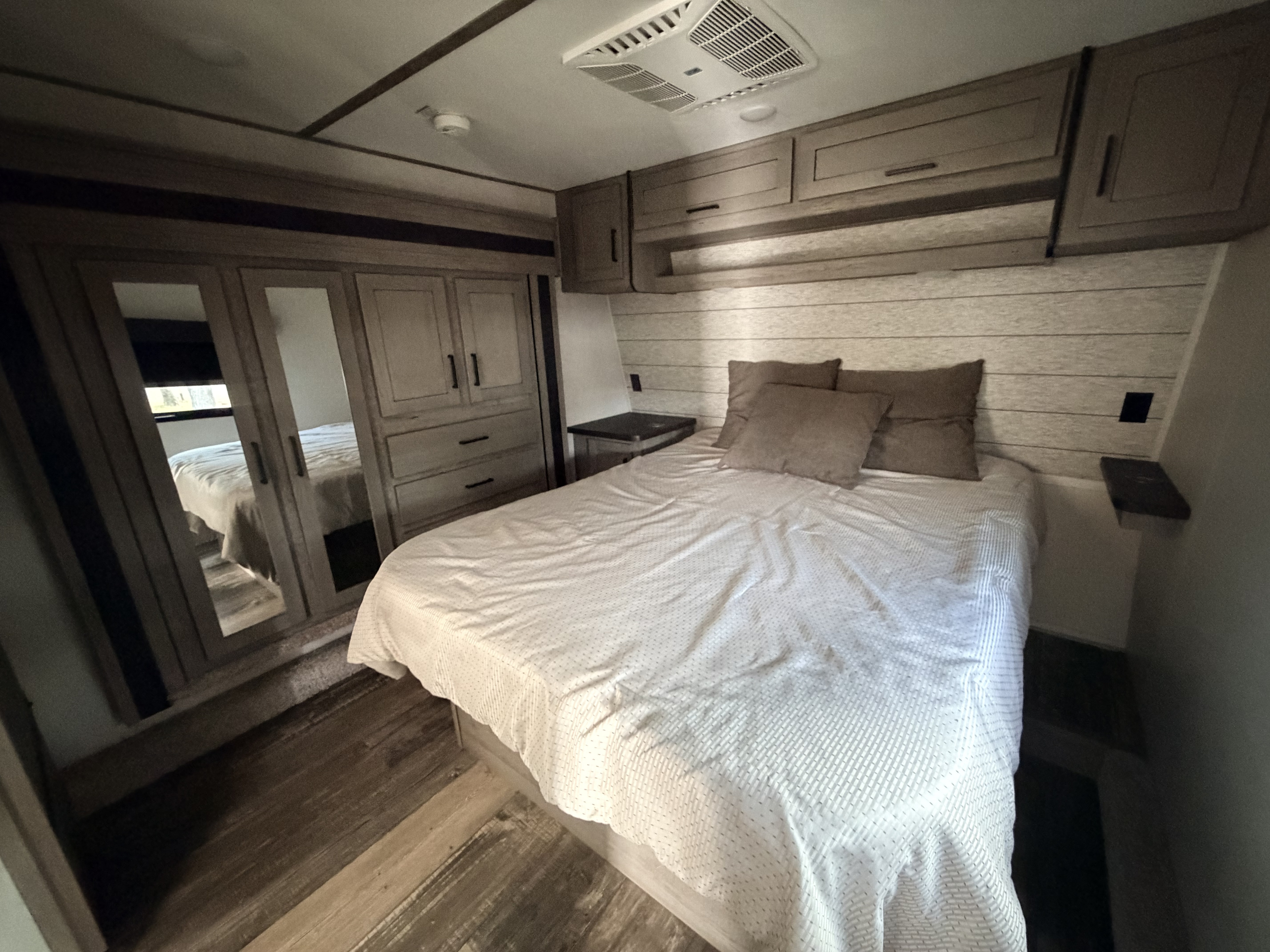 Inside an RV rental: a modern bedroom with a comfortable bed, built-in cabinets, mirrored closet, and wood flooring.. Keystone Raptor 2021