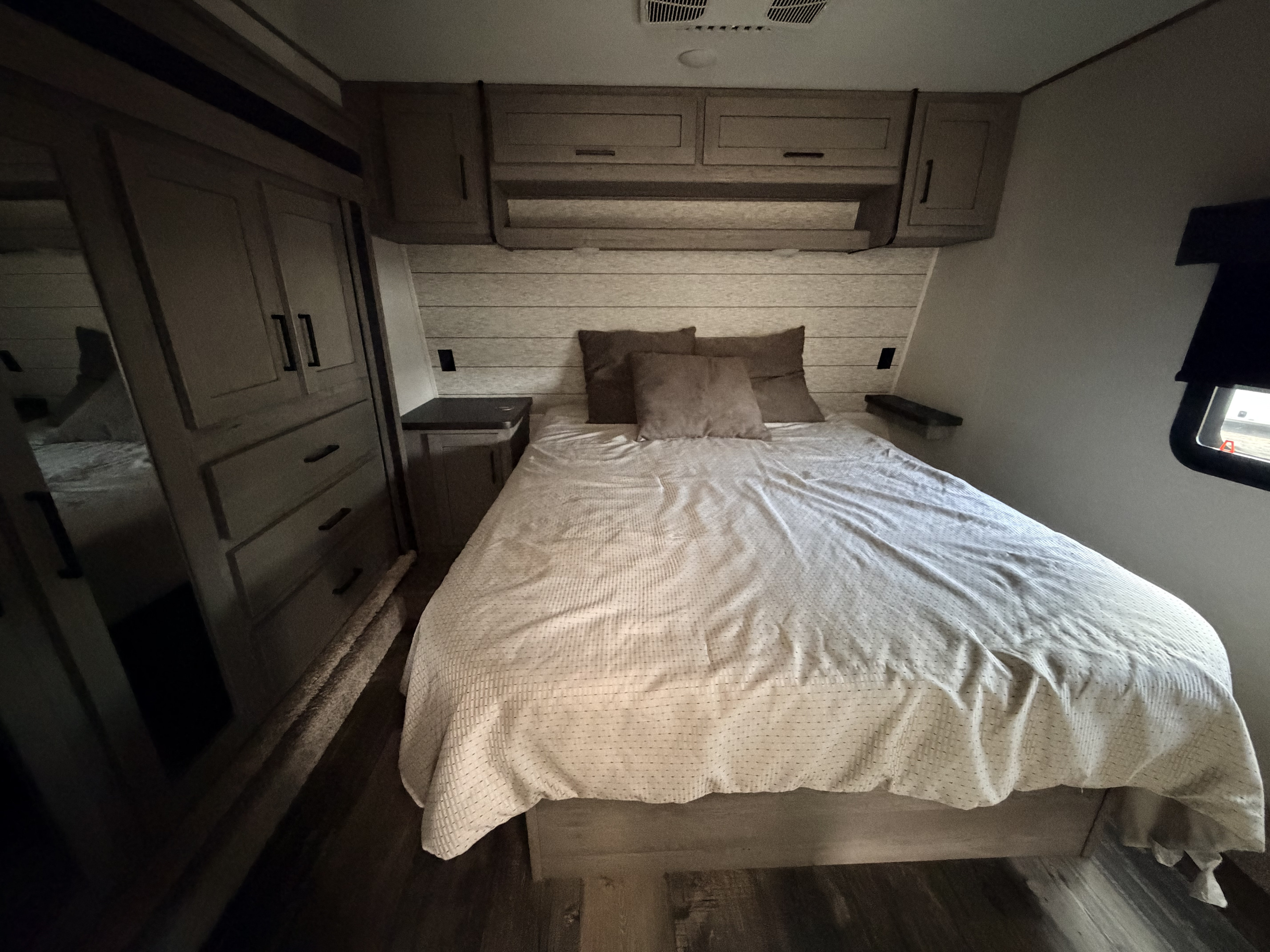 Experience comfort in this RV rental bedroom: a cozy bed with pillows, overhead storage, and a stylish wardrobe with mirrored doors.. Keystone Raptor 2021