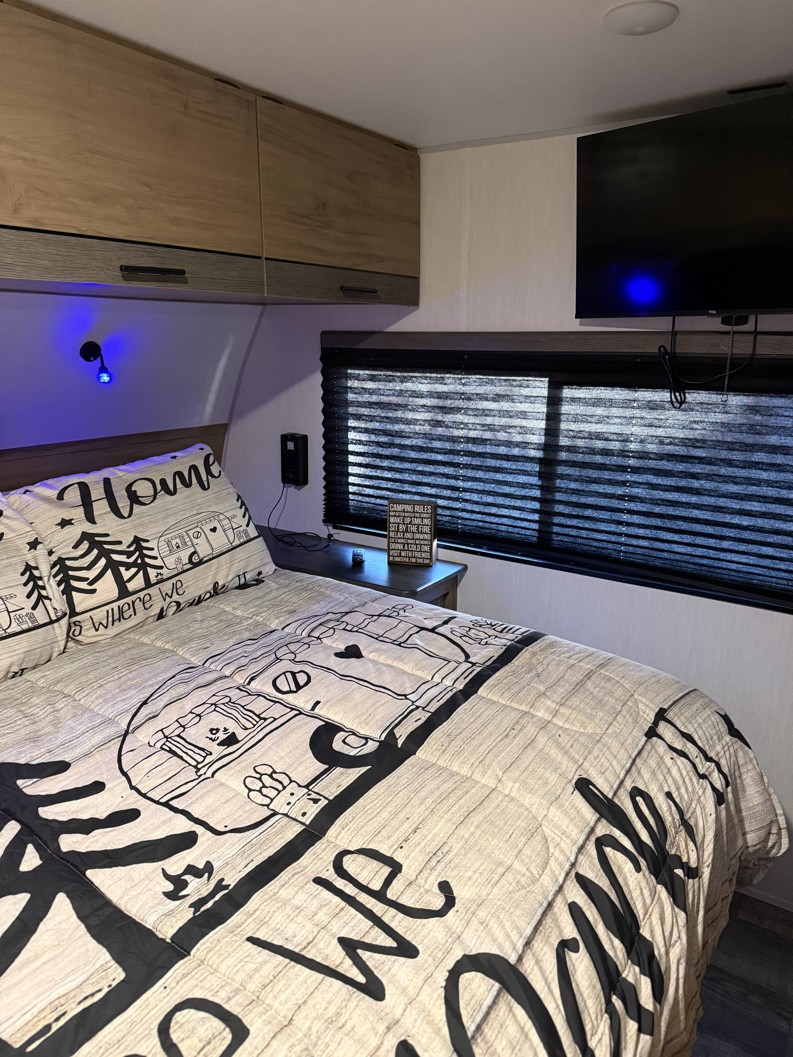 Inviting RV rental bedroom: bed with camping-themed comforter, "Camping Rules" sign on nightstand, TV, and blue ambient light.. Forest River Campsite Reserve 2025
