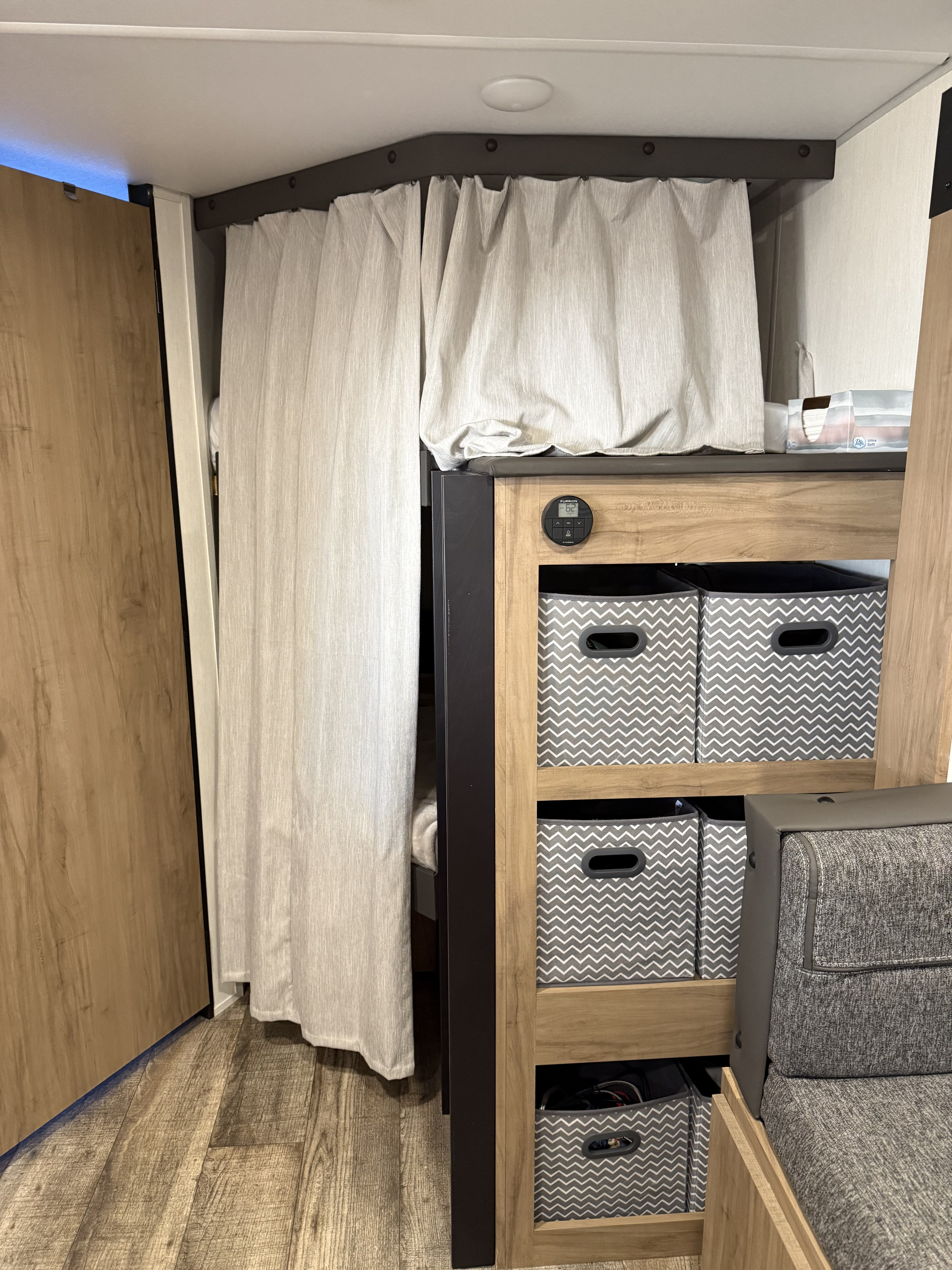 Cozy RV rental interior showcasing bunk beds with privacy curtains, organized storage bins, and a digital thermostat. Perfect for travel comfort.. Forest River Campsite Reserve 2025