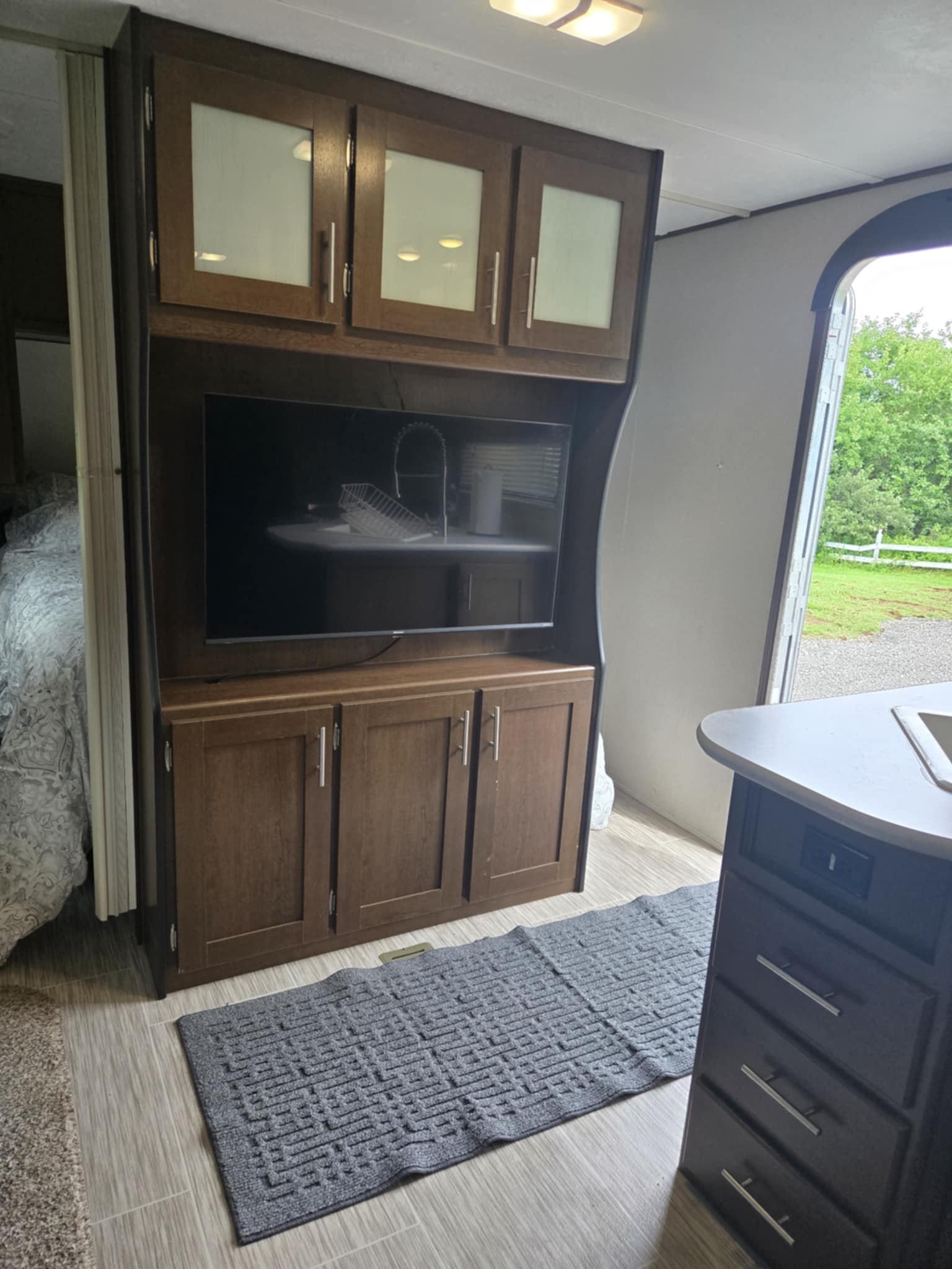RV rental interior: entertainment center with TV & cabinets, glimpse of bedroom & kitchen, open door to green outdoors.. Avenger ATI 2019