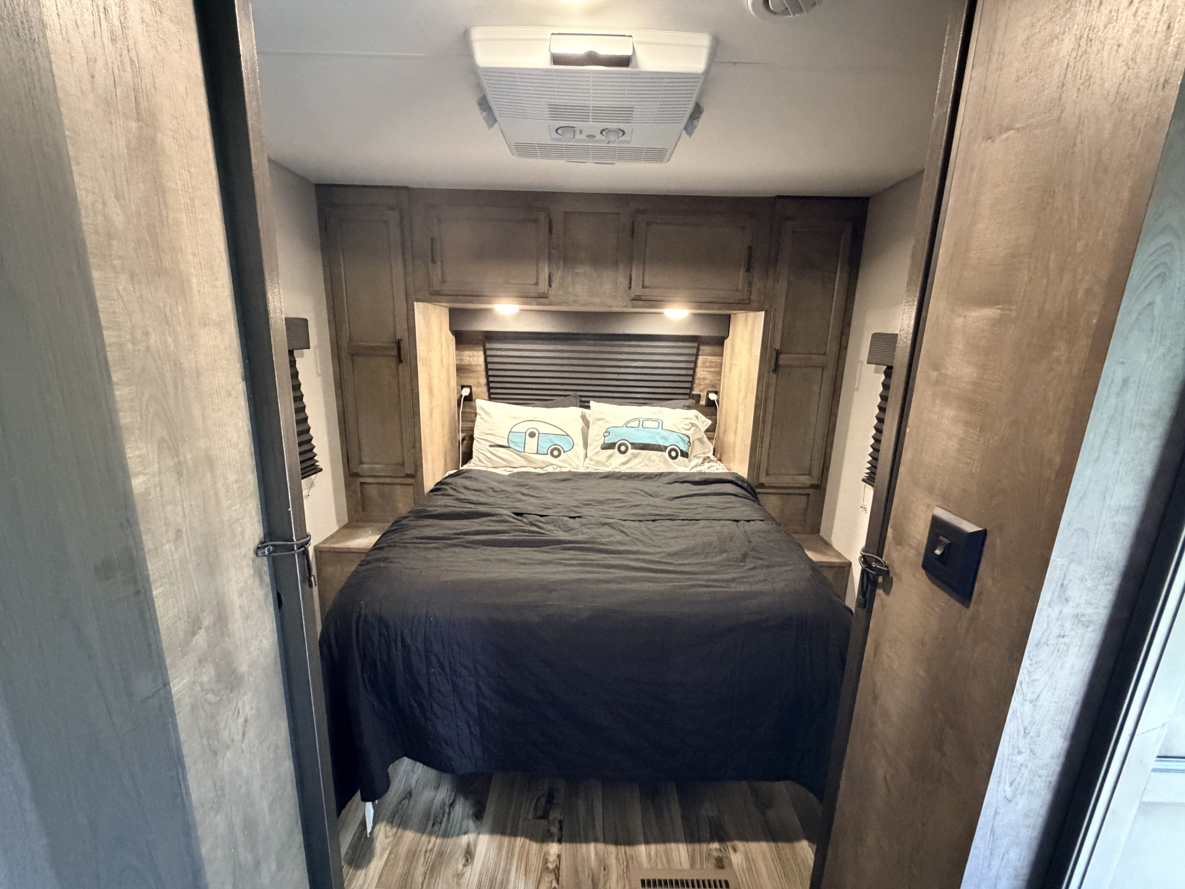 Cozy RV rental bedroom with a made bed, fun camper-themed pillows, overhead cabinets, and an AC unit.. Venture SportTrek ST241VMS 2021