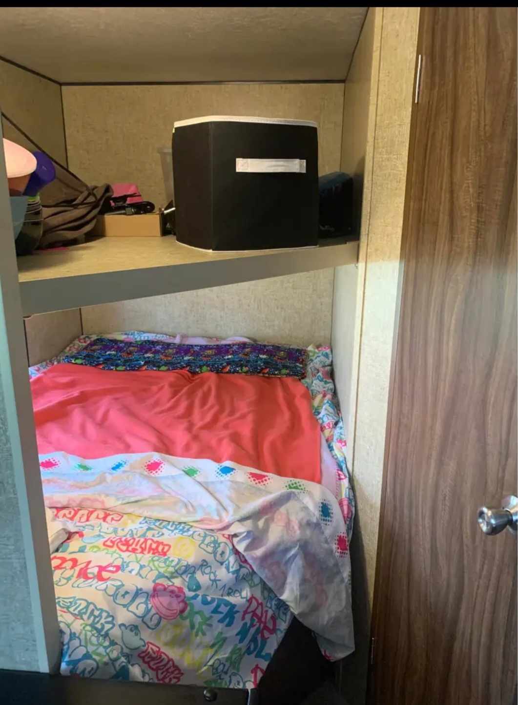 RV rental bunk bed with colorful bedding and overhead storage, showing a compact sleeping area within a camper.. Sportsmen Sportsmen Trailer 2017
