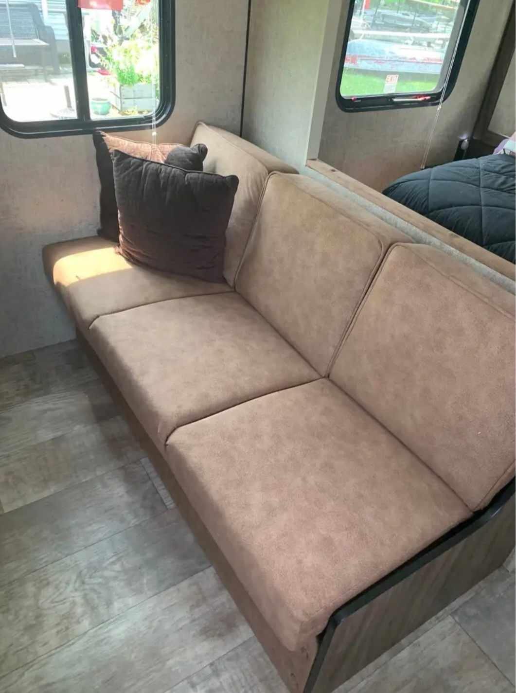 Cozy RV rental interior with a comfortable beige sofa, dark throw pillows, a large window, and a bed in the background.. Sportsmen Sportsmen Trailer 2017