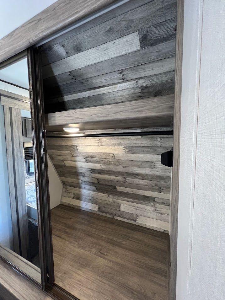 RV rental closet with sliding doors, wood-look walls, a hanging rod, shelf, and light, offering compact storage.. Crossroads RV Zinger 2021