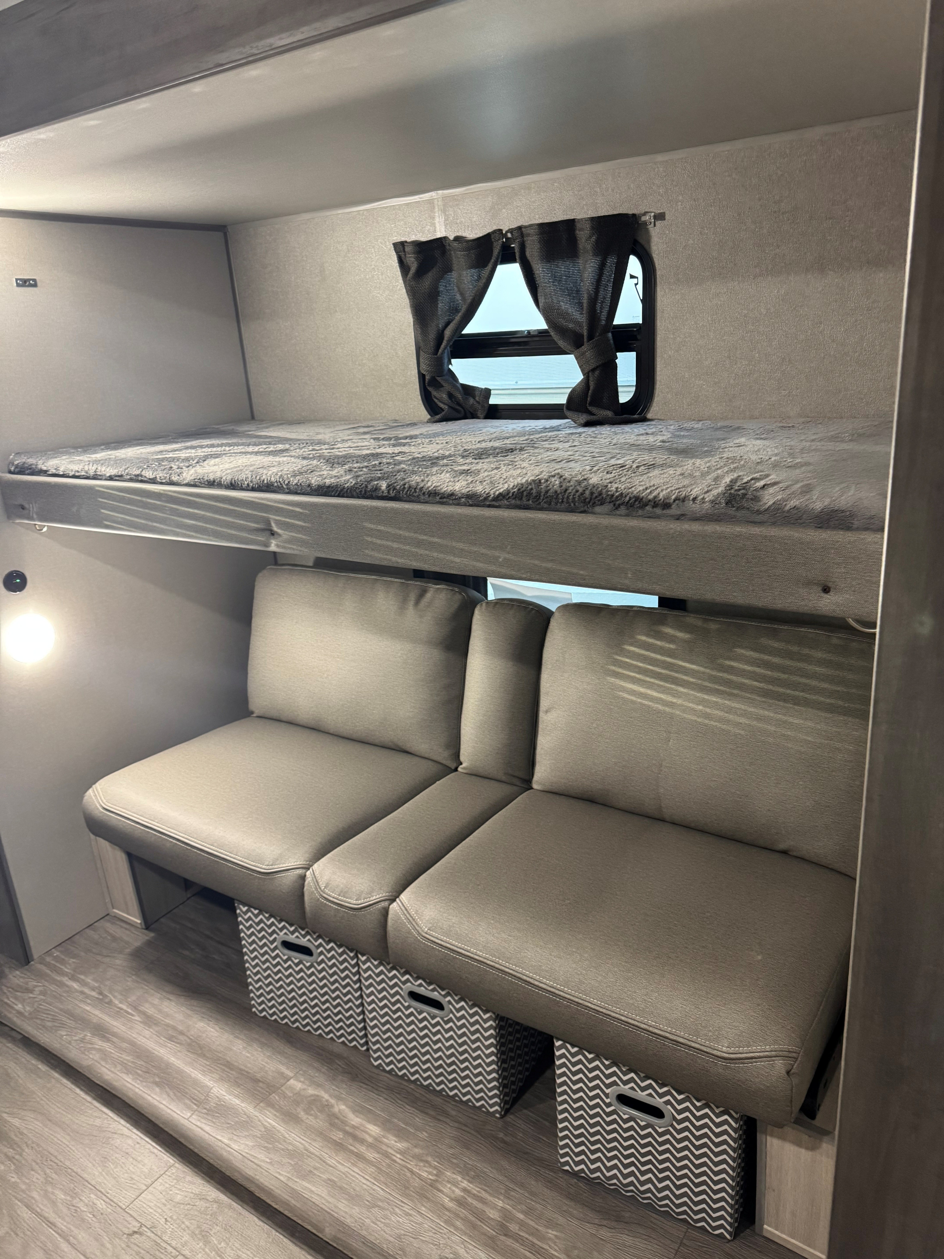 This rv rental features comfy bunk beds, a cozy bench seat with chevron storage, and a window. An inviting interior for travelers.. Forest River Aurora Aurora 2026