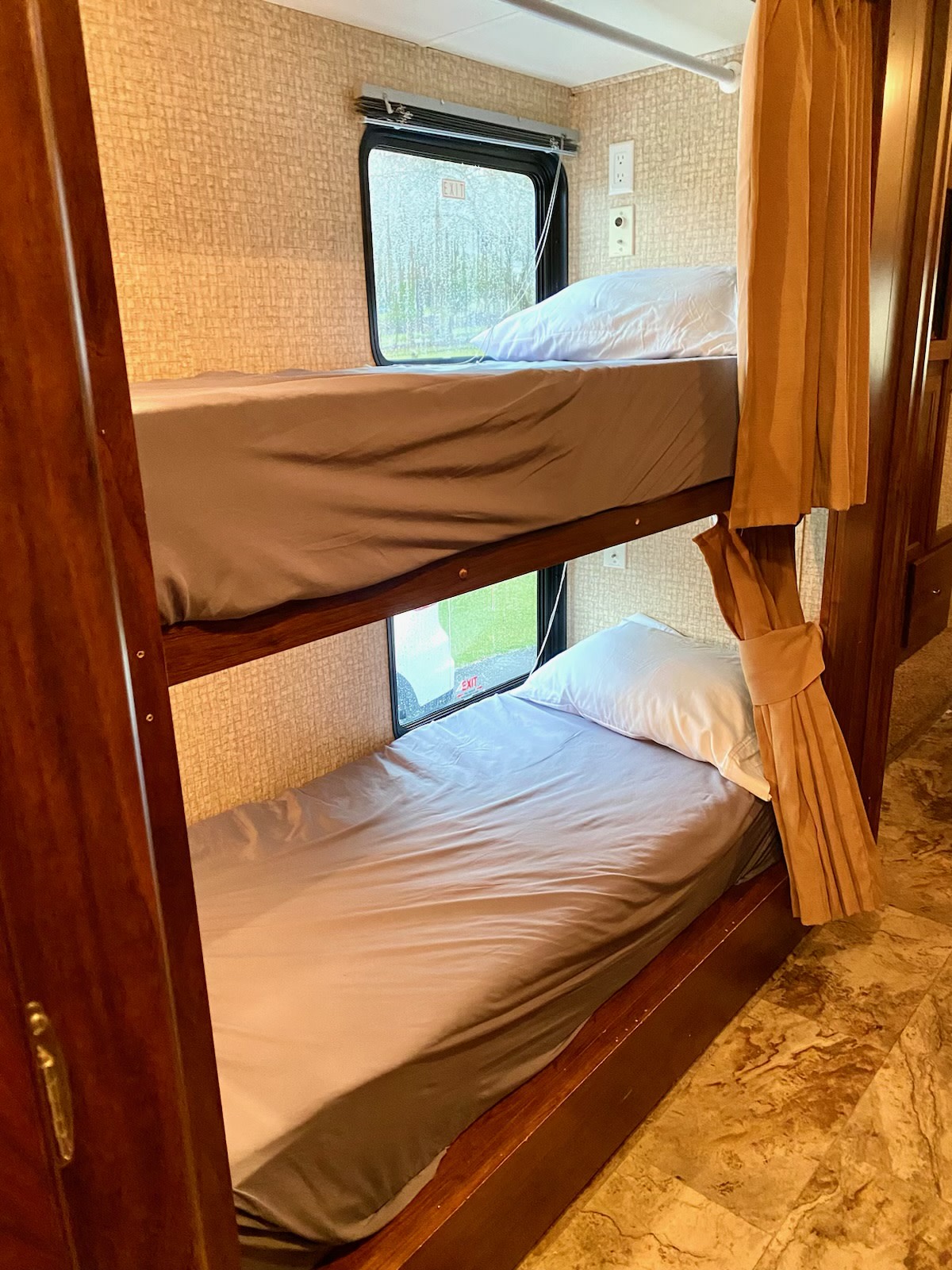 Interior of an RV rental showing two neatly made bunk beds with windows, an 'EXIT' sign, and privacy curtains.. Coachmen Pursuit 33 Bh 2016