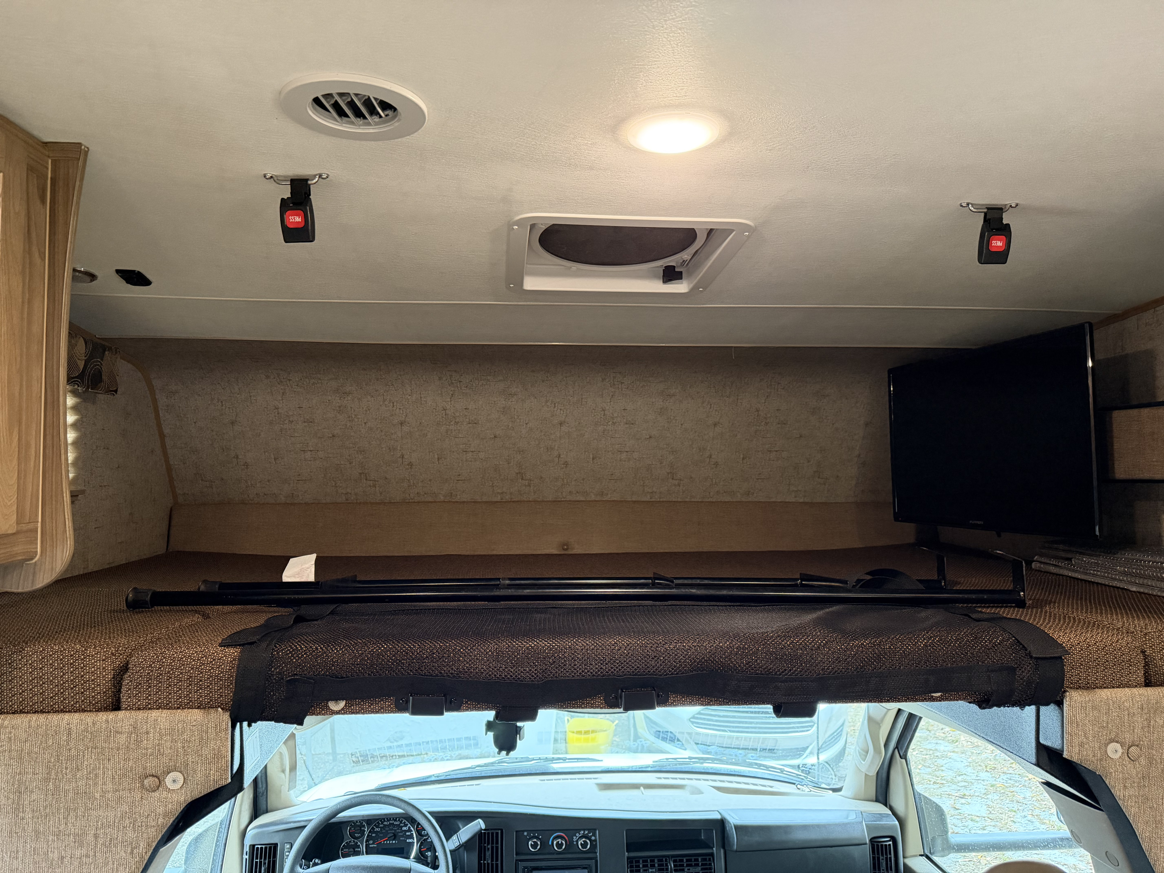 RV rental interior: Over-cab sleeping area with safety net, TV, ceiling vents, and driver's cabin below.. Coachmen Freelander 26 RS 2017