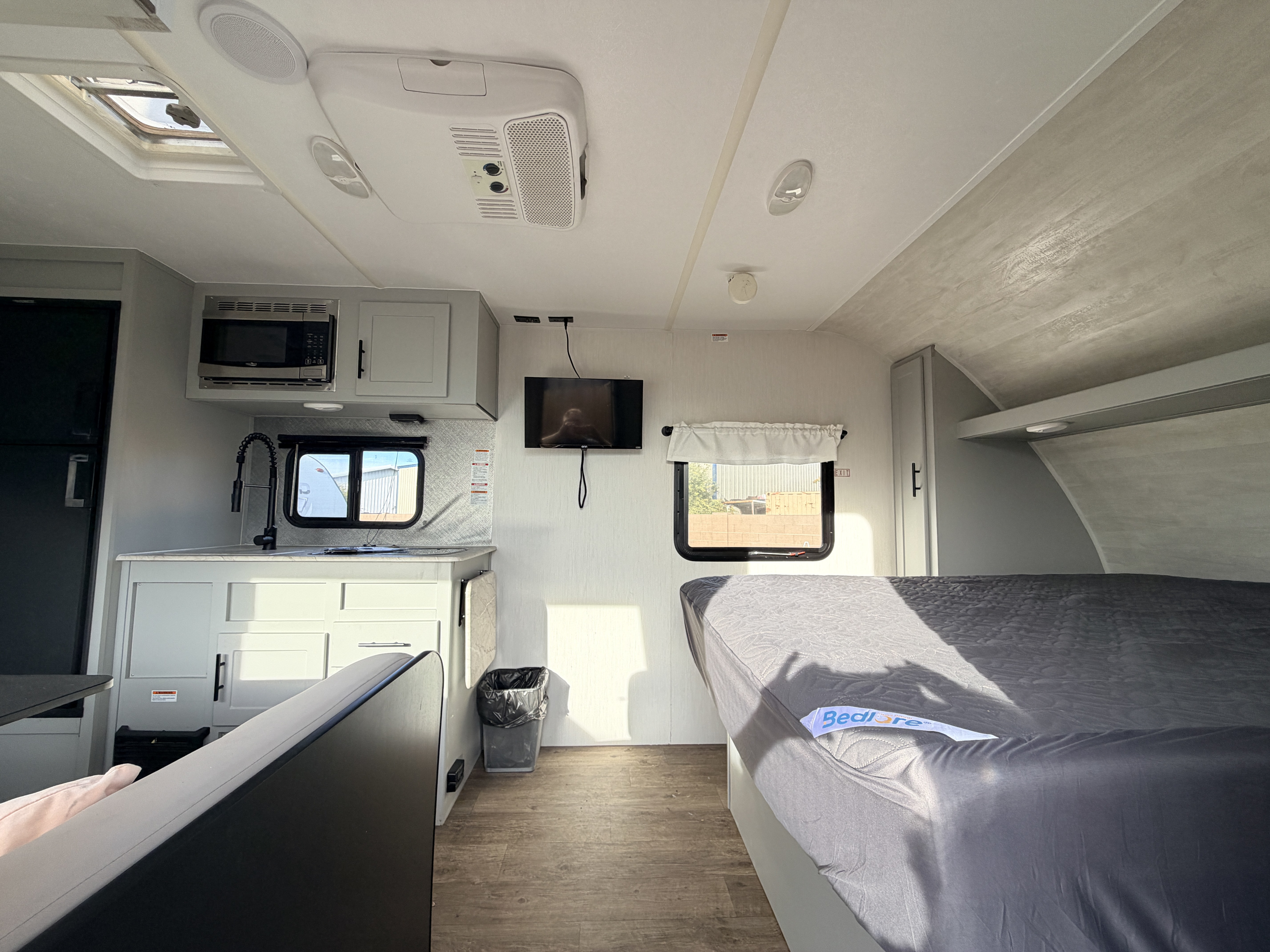 Clean rv rental interior. Features a compact kitchen with microwave, sink, TV, and a neatly made bed. Bright and airy.. Forest River Vibe 2021