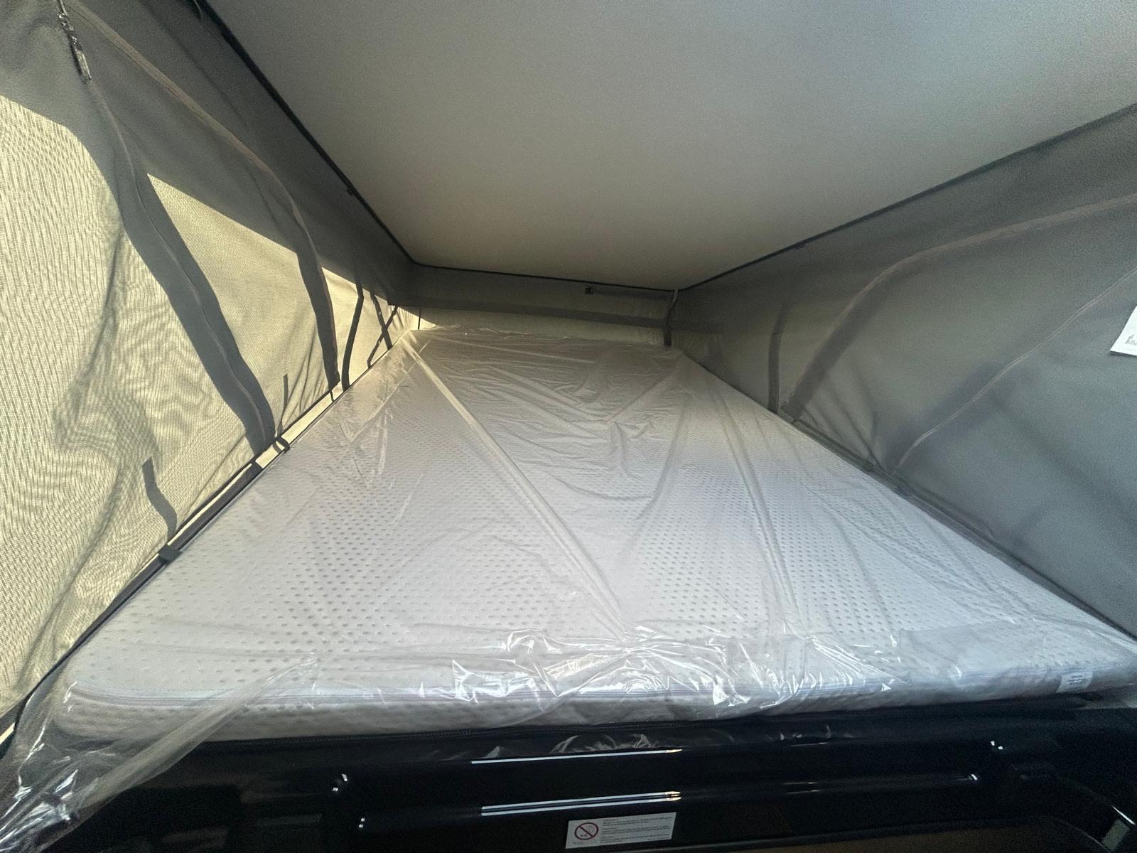 RV rental pop-top bed: a new, plastic-wrapped mattress under the extendable roof, with mesh window walls for ventilation.. Sunlight Vanlife 540 2026
