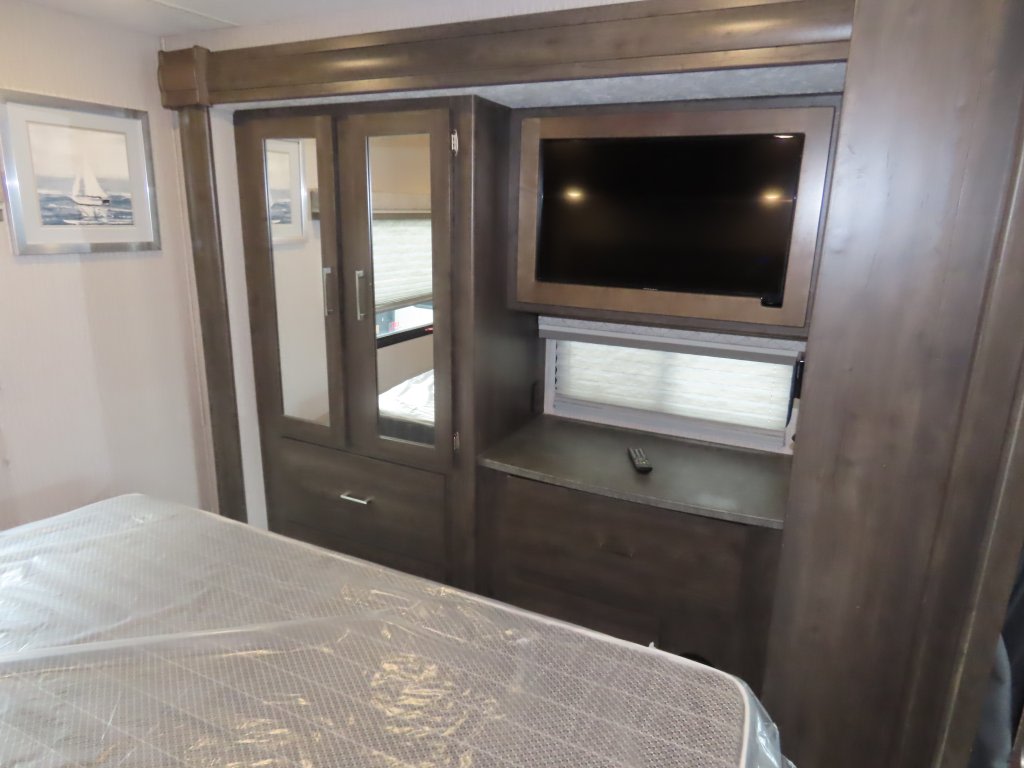 Inside an RV rental, this bedroom features a bed with plastic covering, a mirrored wardrobe, TV, and a window.. Coachmen PURSUIT 31BH 2023