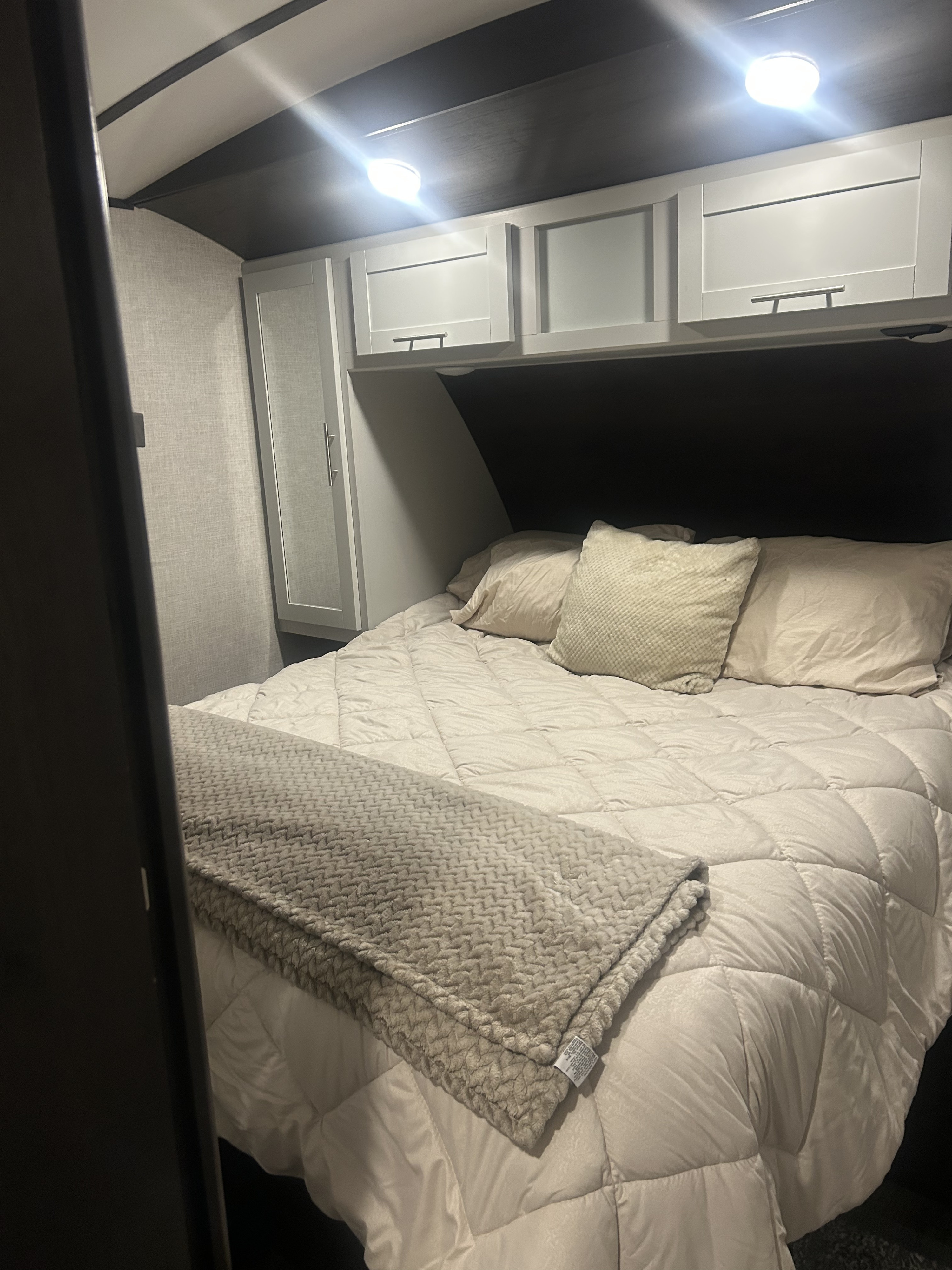 Cozy rv rental bedroom with light bedding, overhead cabinets, and bright lighting for a comfortable stay.. Keystone RV 24RKPR 2020
