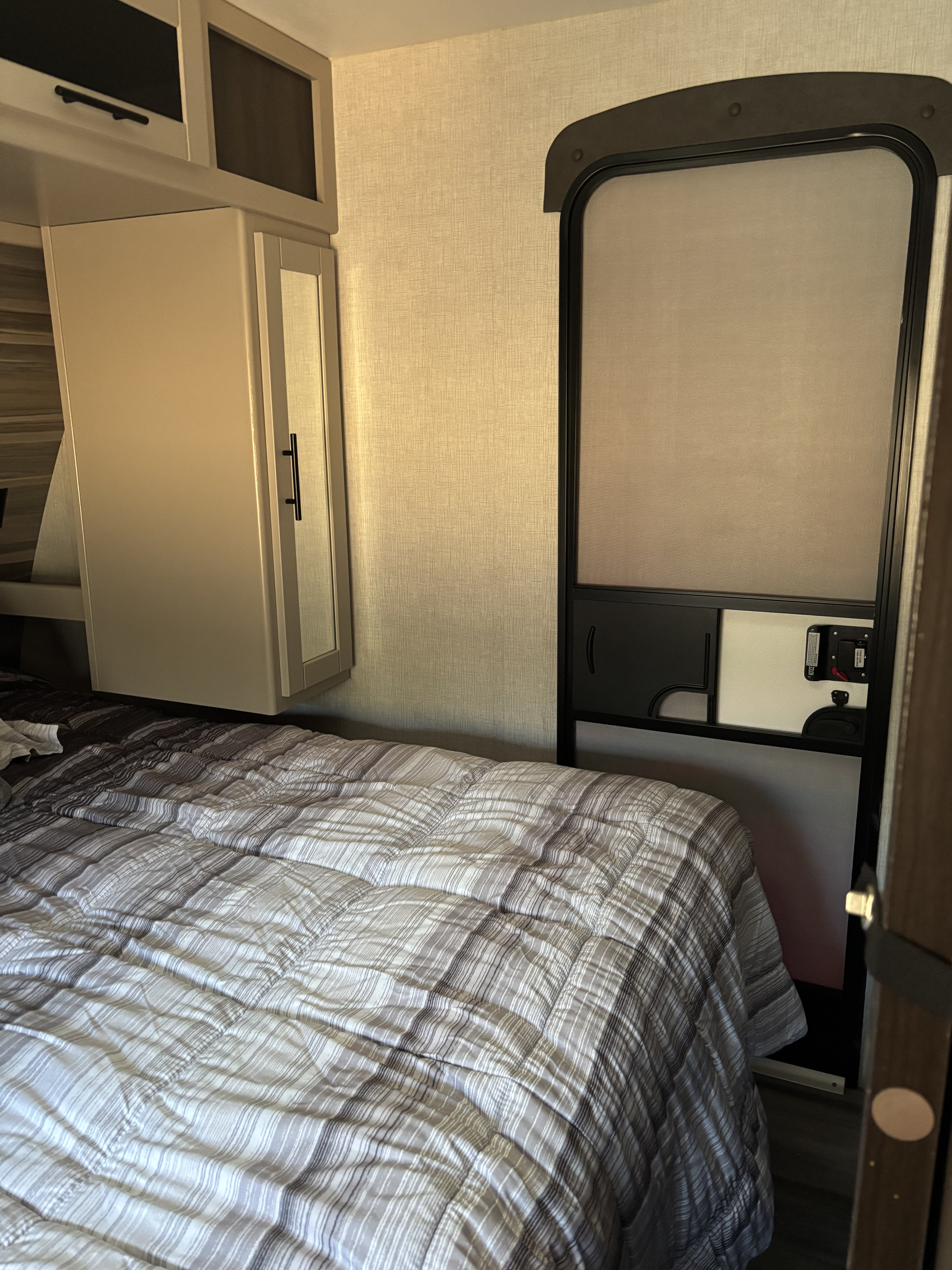 Cozy RV rental bedroom with striped bedding, overhead cabinets, and an entrance door. Perfect for travel adventures.. Crossroads RV Cruiser Aire 2022