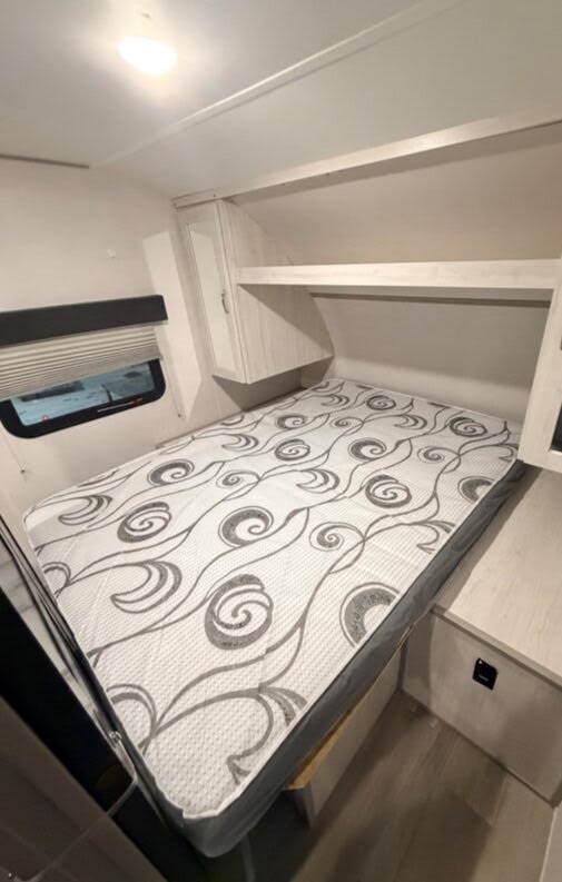 Cozy RV rental bedroom featuring a patterned mattress, overhead shelves, a mirrored cabinet, and a window for comfortable travel.. Forest River Tracer 2022