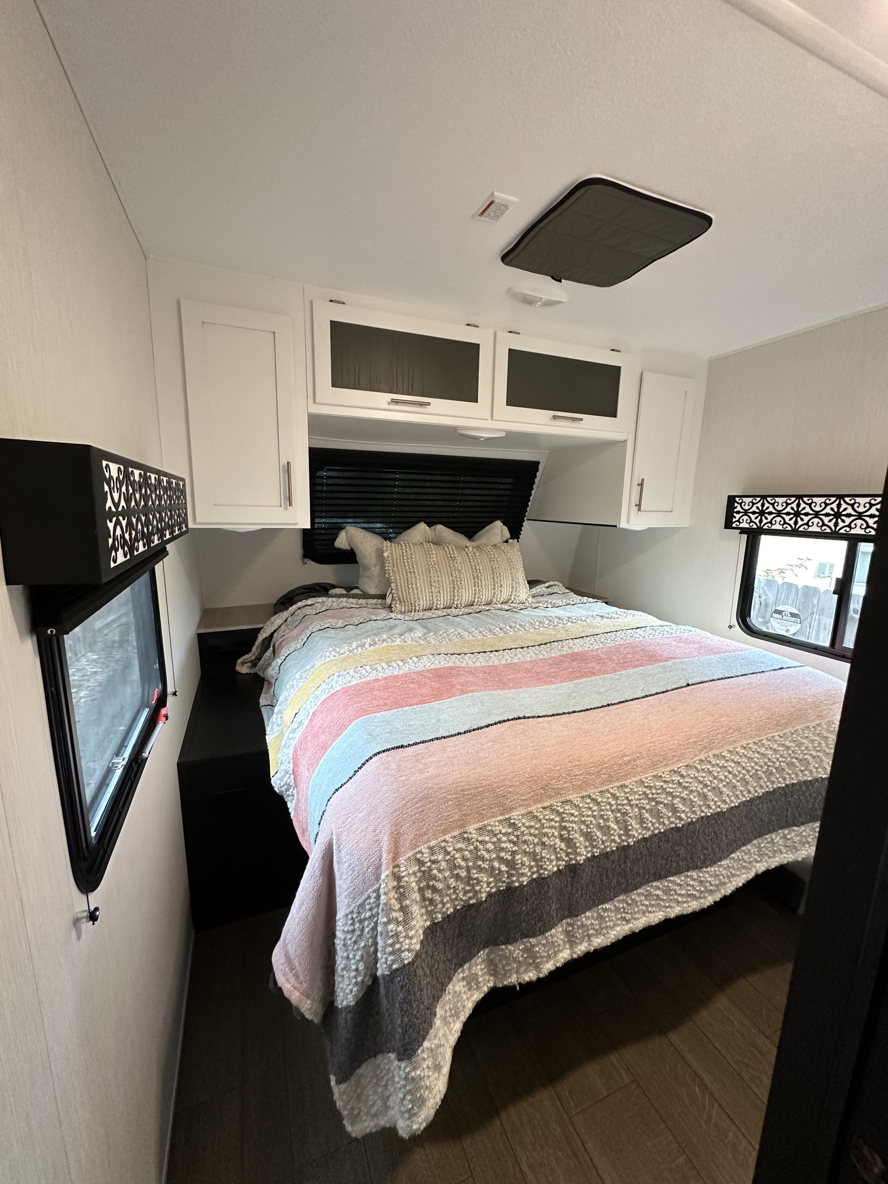 Cozy RV rental bedroom with colorful bed, overhead cabinets, and side windows for comfortable stays.. Forest River Wildcat 247 RKX 2022