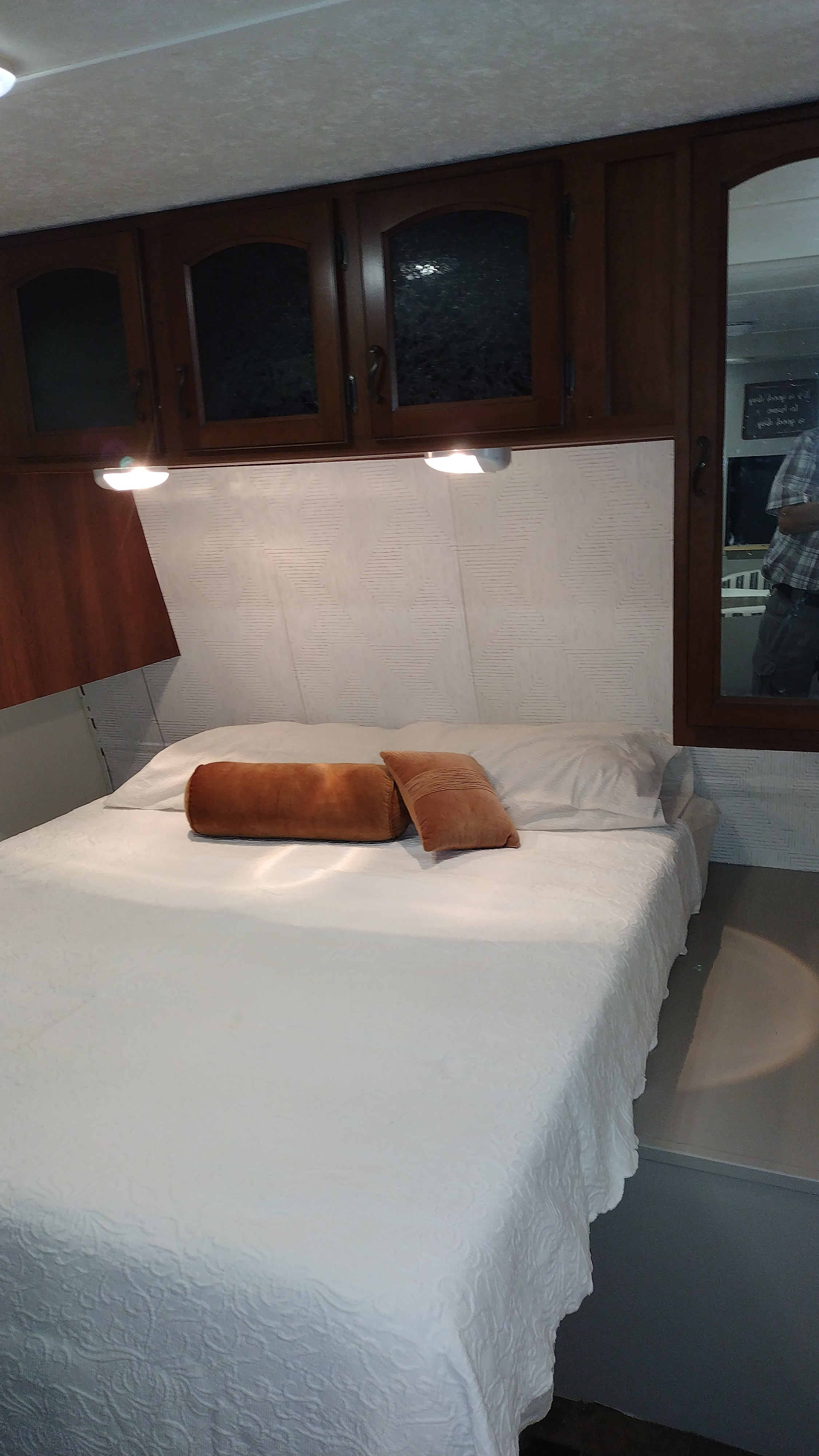 Inside an RV rental: a neat bedroom with a white bed, brown accent pillows, overhead cabinets, and soft lighting.. Avenger Avenger 2012
