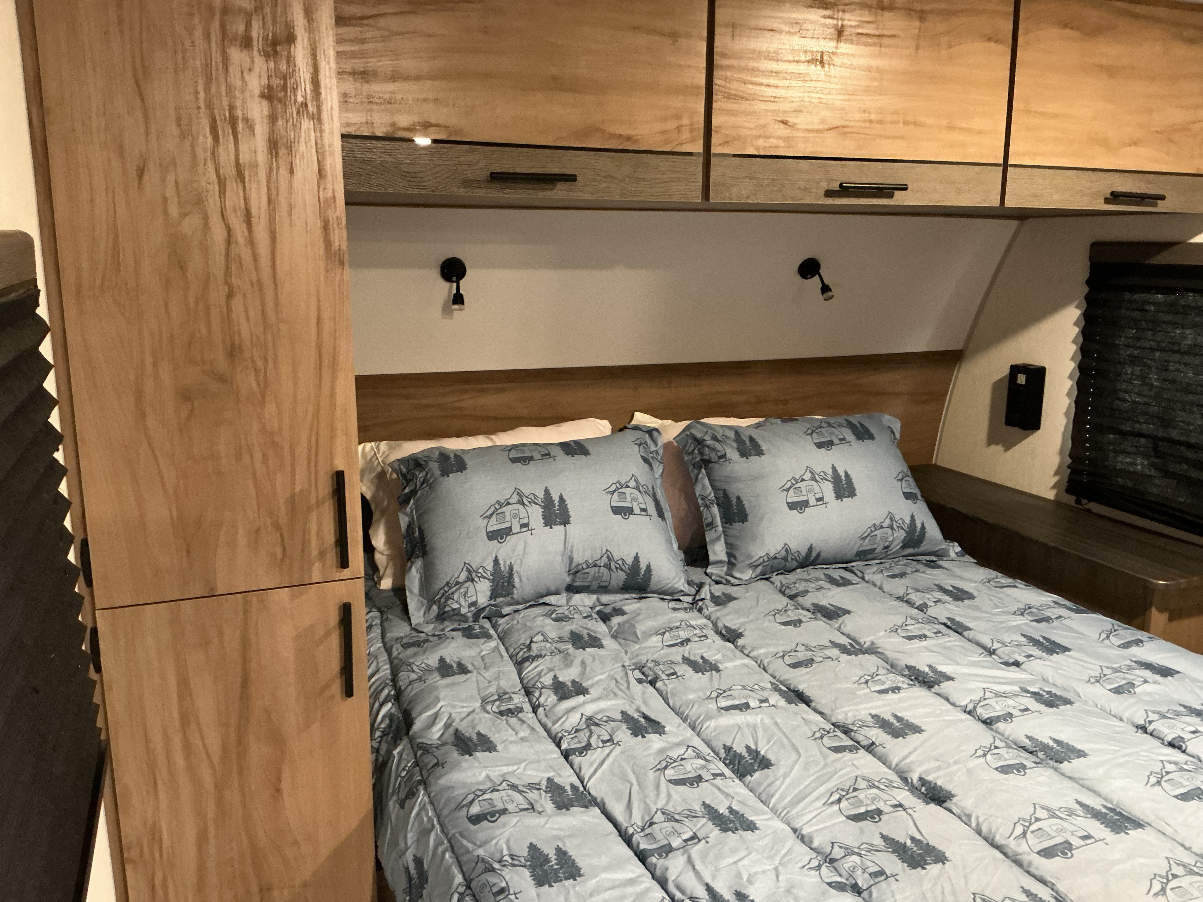 Cozy RV rental bedroom with a bed featuring camper and mountain-themed bedding, wooden cabinets, and wall lights.. Forest River Campsite Reserve 2025