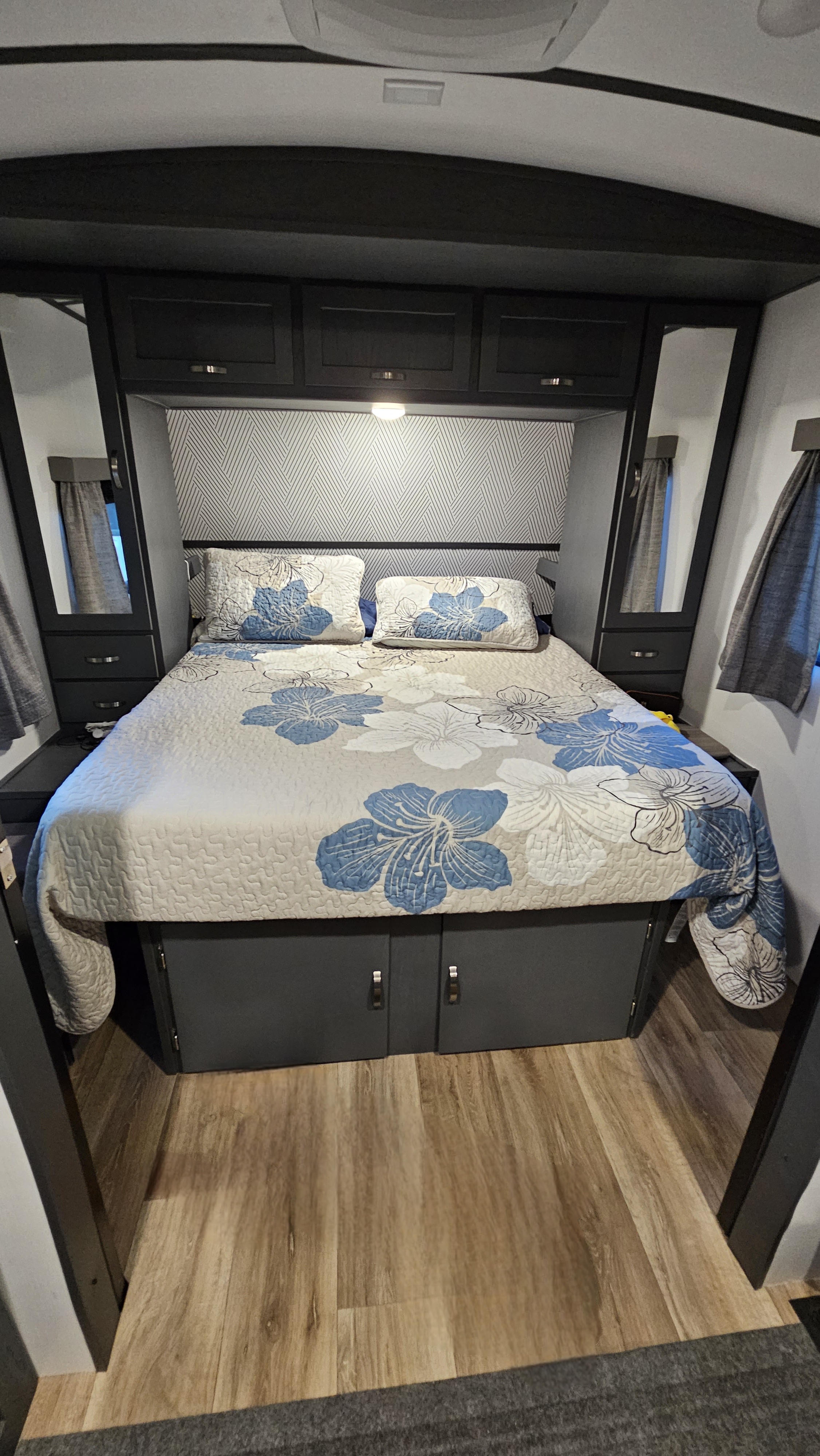 Compact rv rental bedroom with floral queen bed, overhead cabinets, and clever side storage solutions.. Keystone RV Bullet Ultra Lite 2022