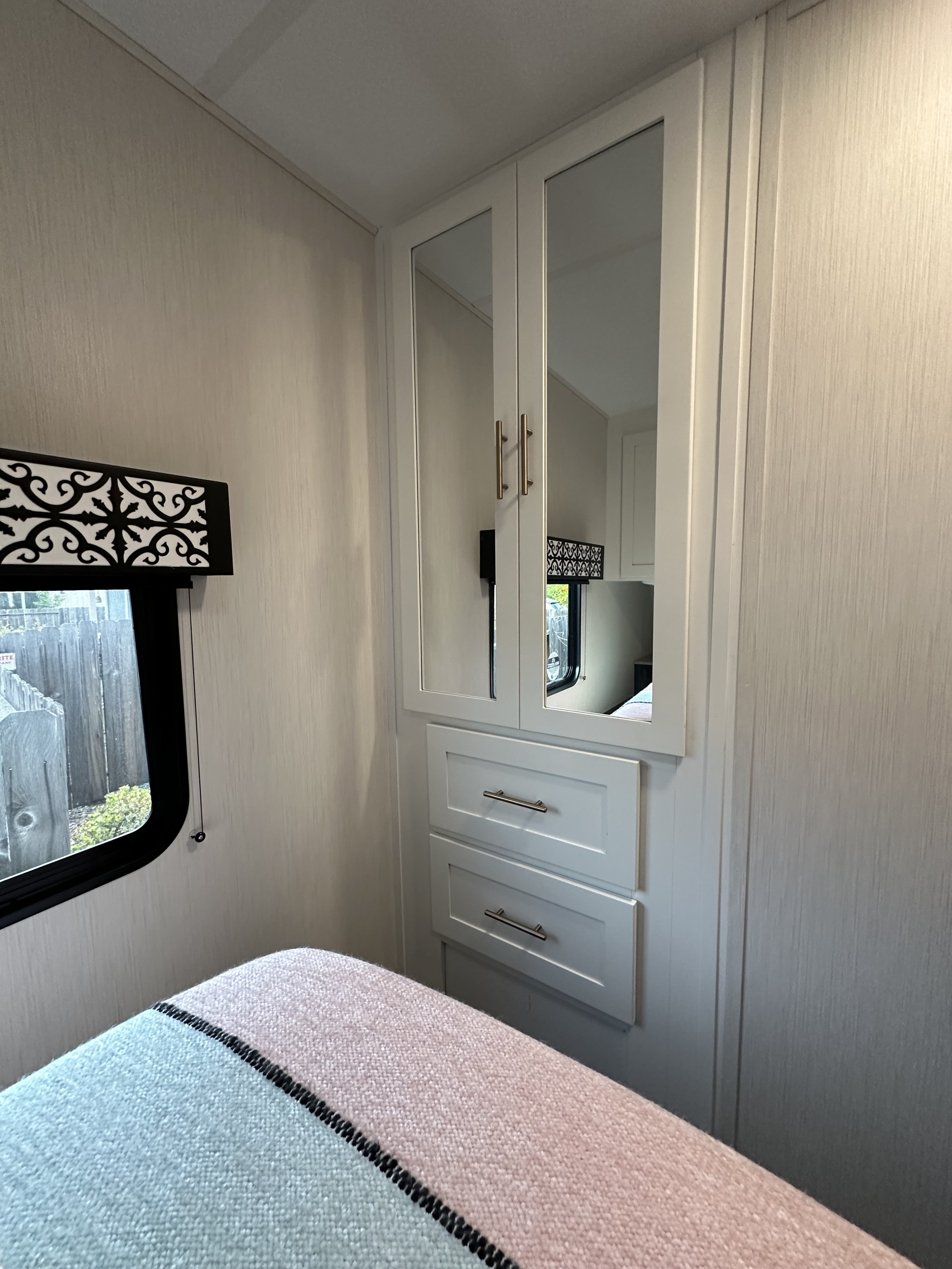 Bright RV rental bedroom showing a mirrored wardrobe with drawers, a window, and a bed with a blue and pink striped blanket.. Forest River Wildcat 247 RKX 2022