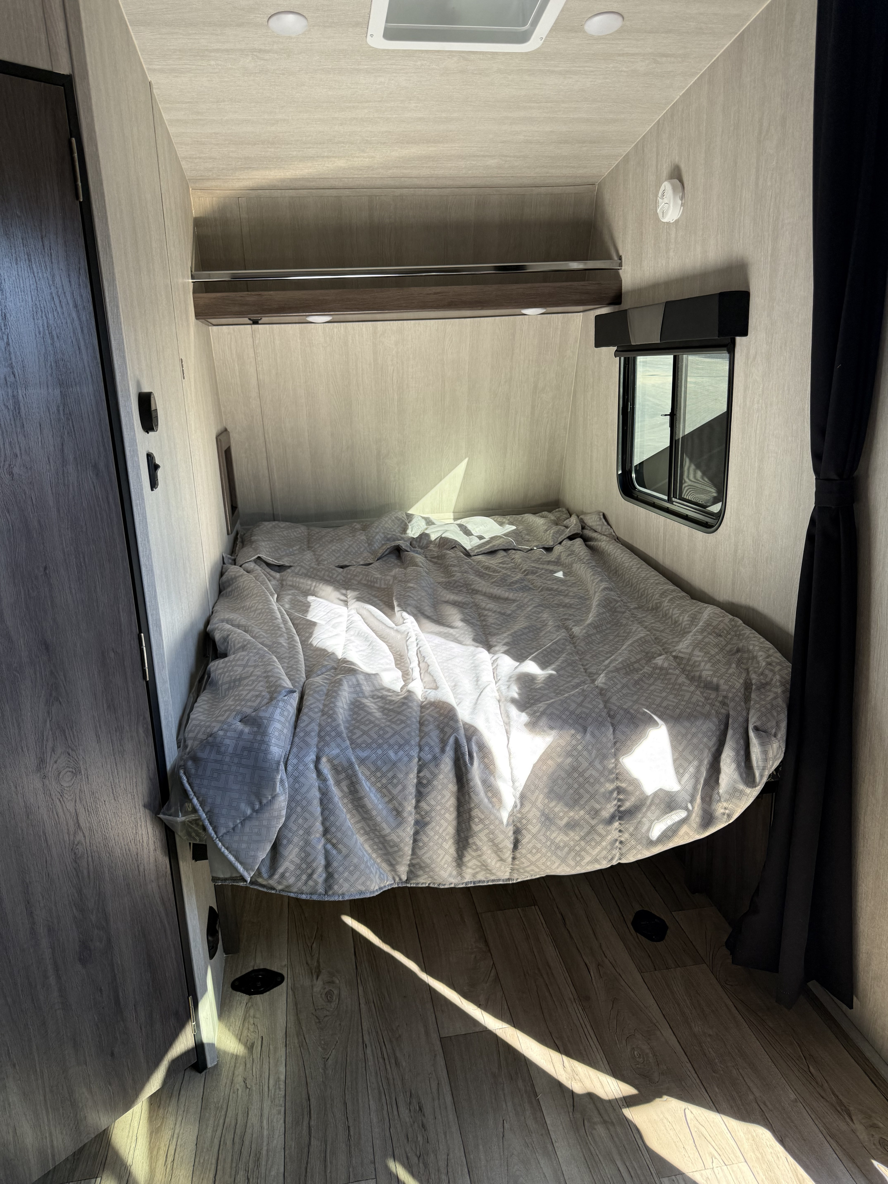 Inside a comfy RV rental bedroom: gray bed, wood-paneled walls, window, and bright sunlight.. Genesis Supreme Rv Genesis Supreme 2026