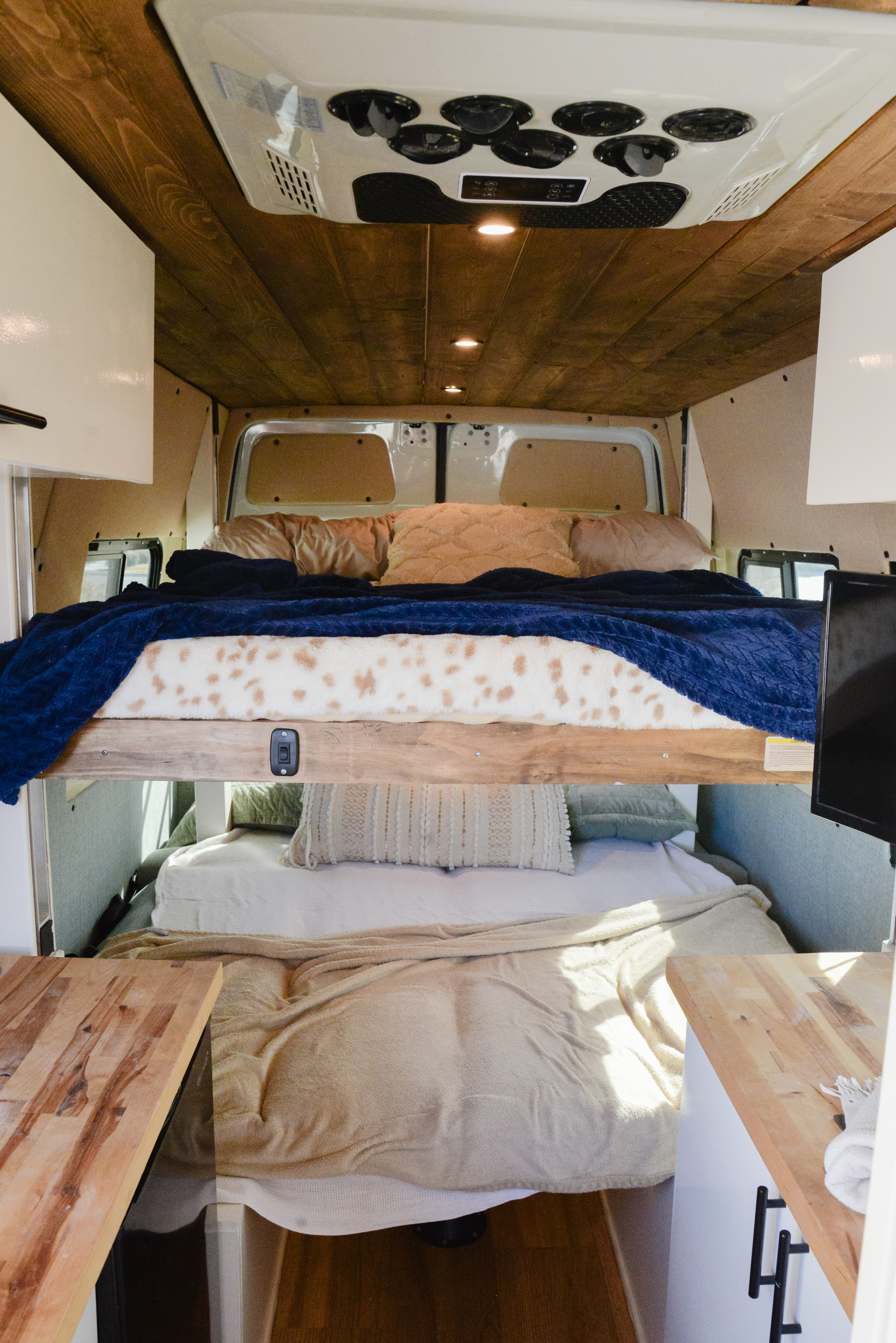 RV rental camper van interior with stacked bunk beds, wood ceiling, and warm lighting. Perfect for road trips!. Mercedes Sprinter 2022