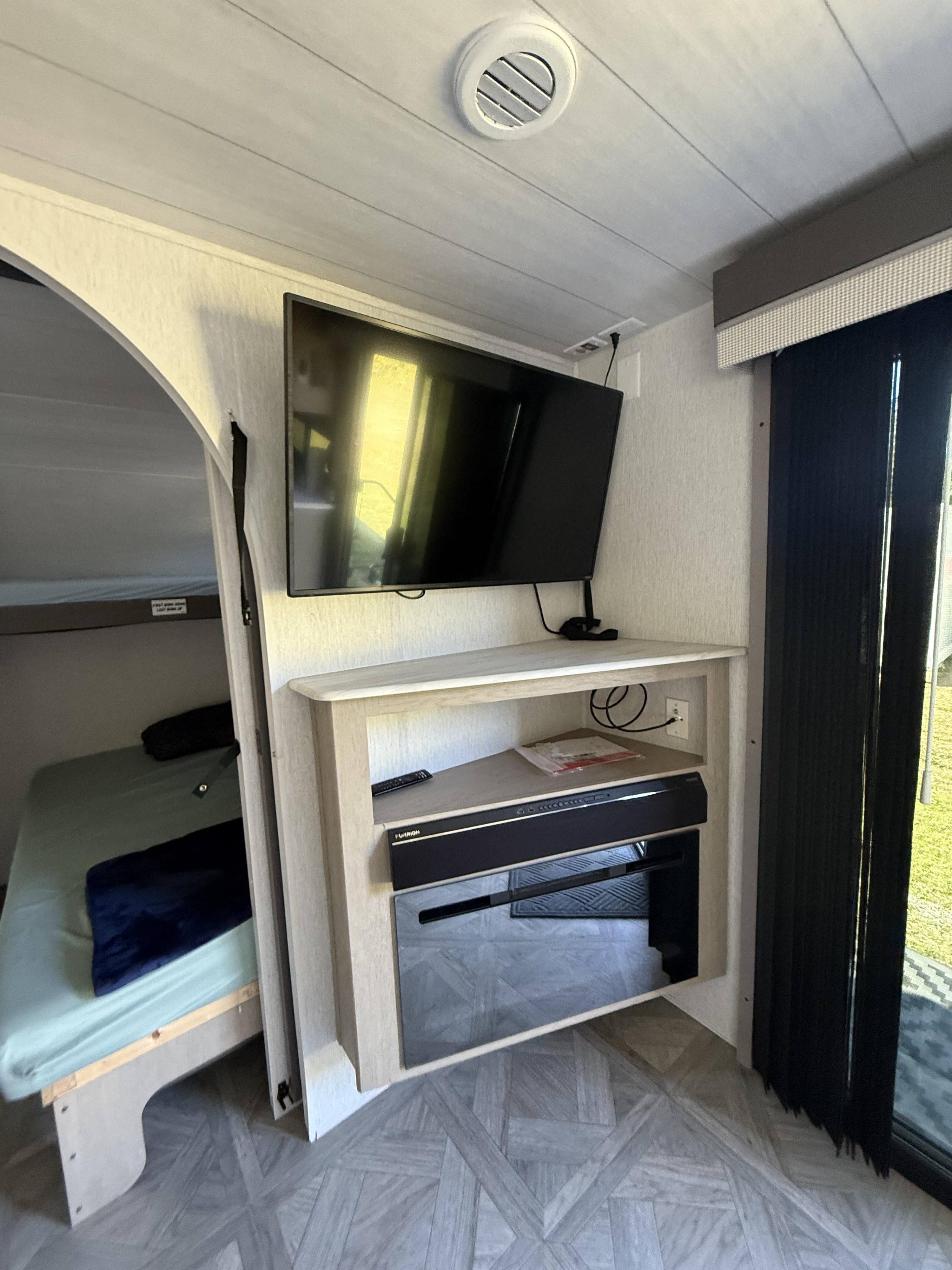 RV rental interior: bunk bed, flat-screen TV, and entertainment unit with a Furrion soundbar. Green grass visible outside.. Salem 36VBDS 2023