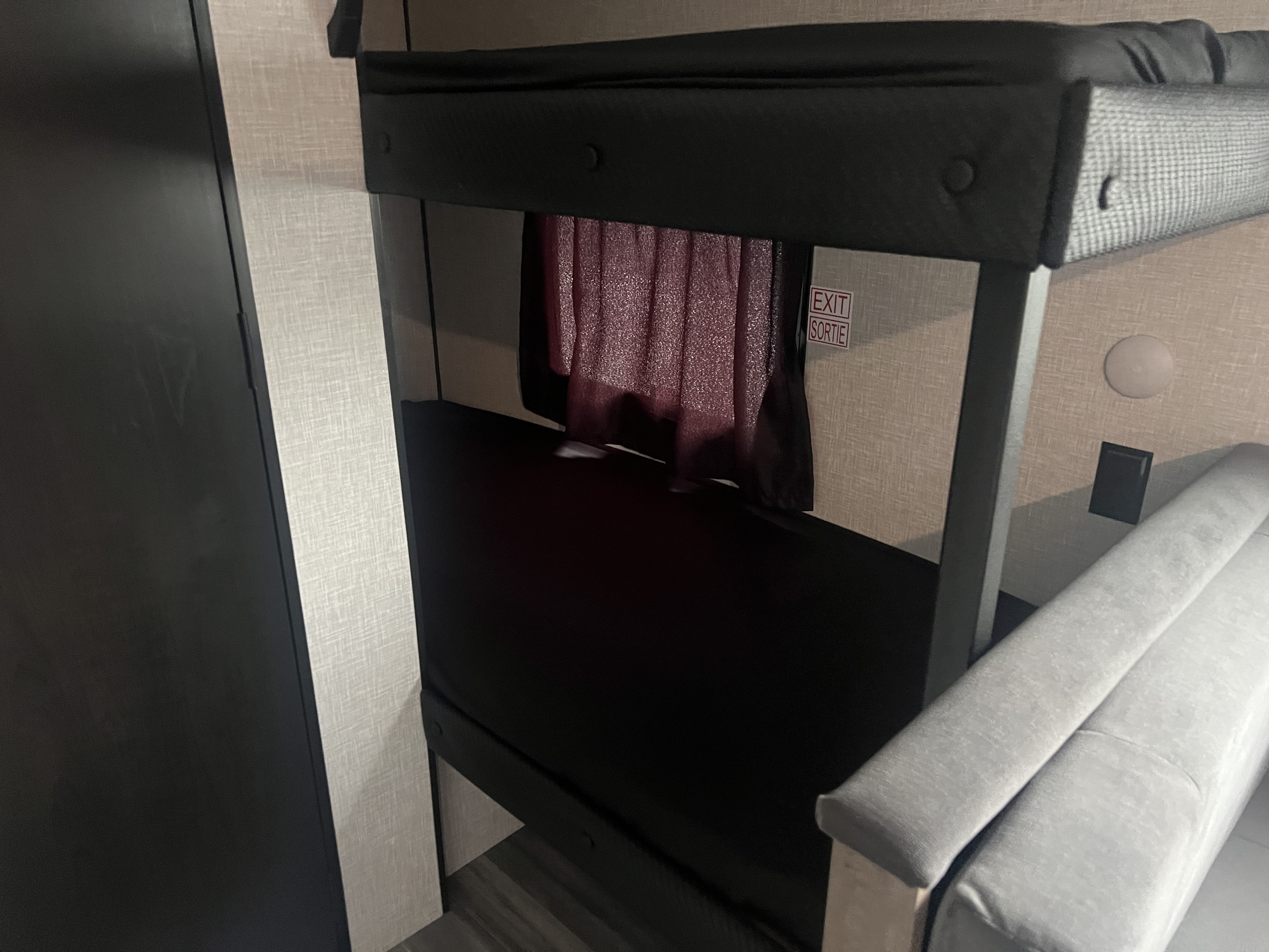 RV rental: view of a cozy sleeping area with bunk beds, dark mattresses, a red curtain, exit sign, and part of a grey sofa.. Jayco Jay Flight SLX Baja Edition 2025