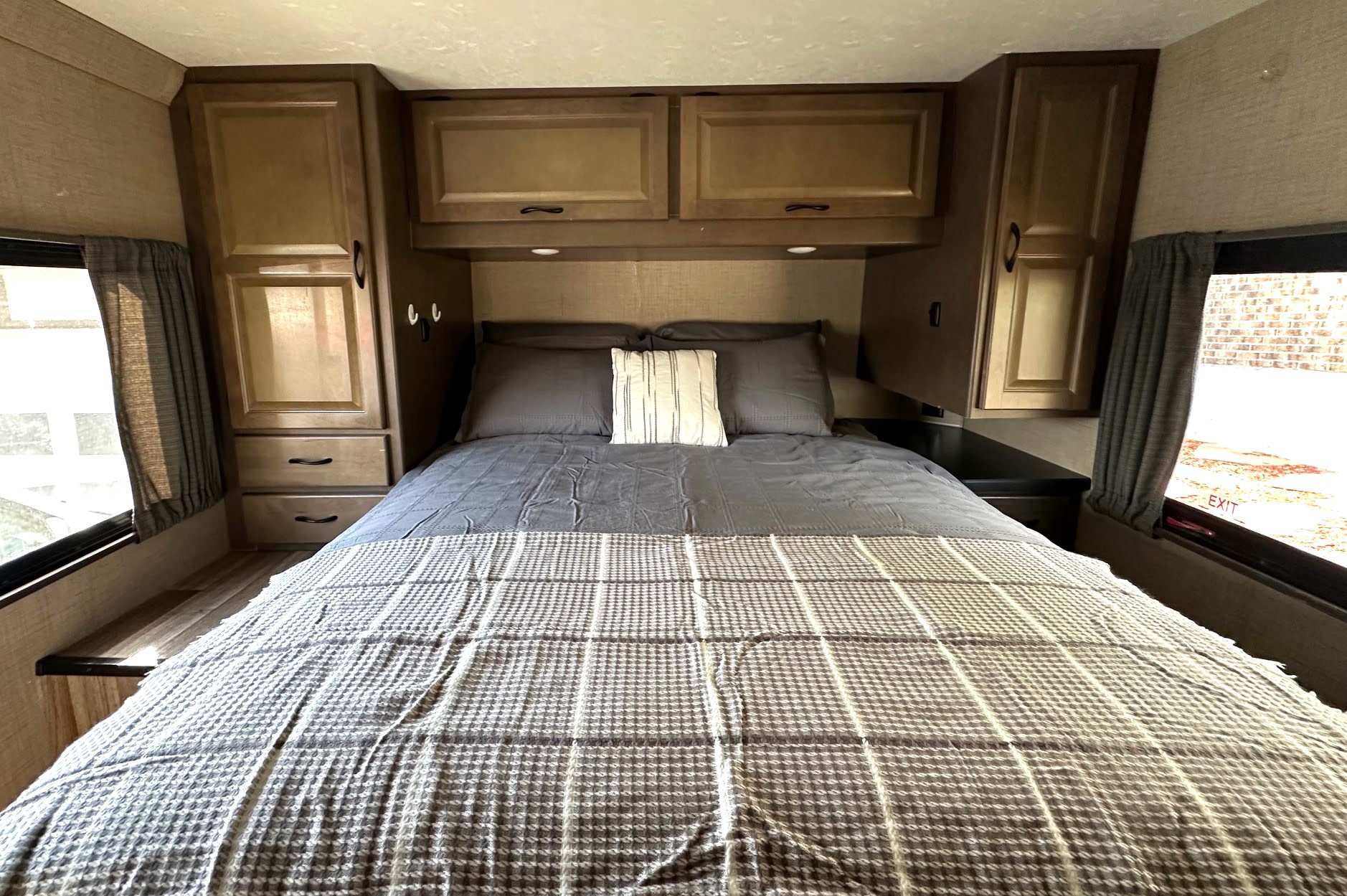 Inviting rv rental bedroom with a large bed, dark gray bedding, a striped pillow, wooden cabinets, and window views.. Thor Majestic 2019