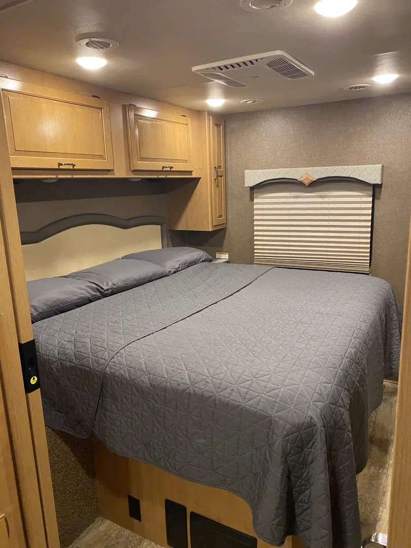 Cozy RV rental bedroom with a comfy queen bed, overhead storage, and AC unit for a relaxing trip.. Thor Hurricane 2017