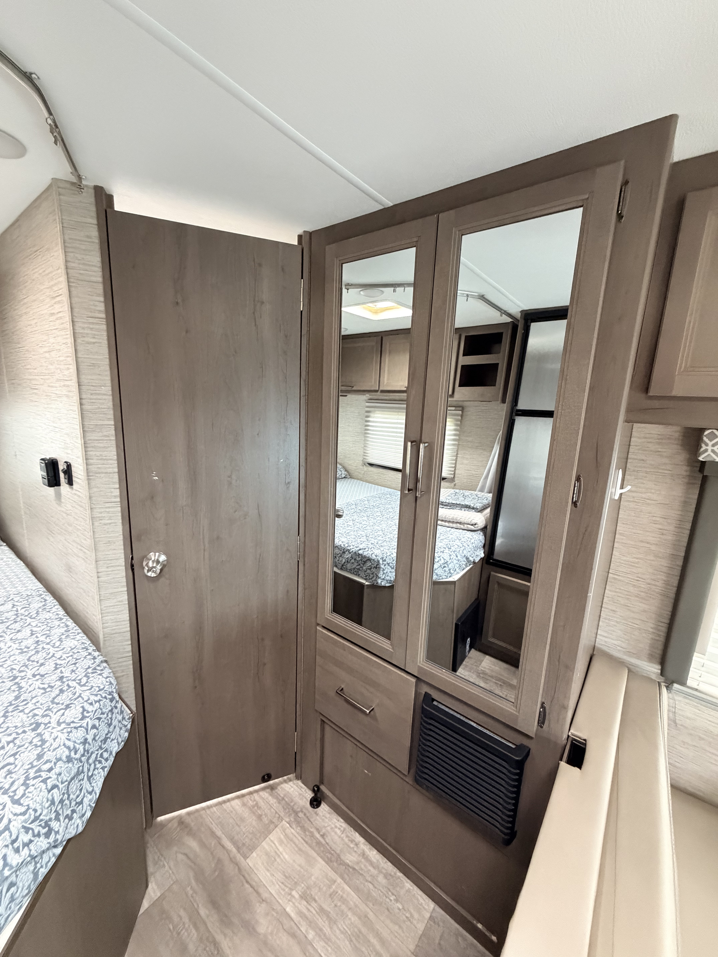 This RV rental showcases a cozy bedroom setup with a patterned bed, mirrored wardrobe, and convenient storage solutions.. Thor Coleman 2023