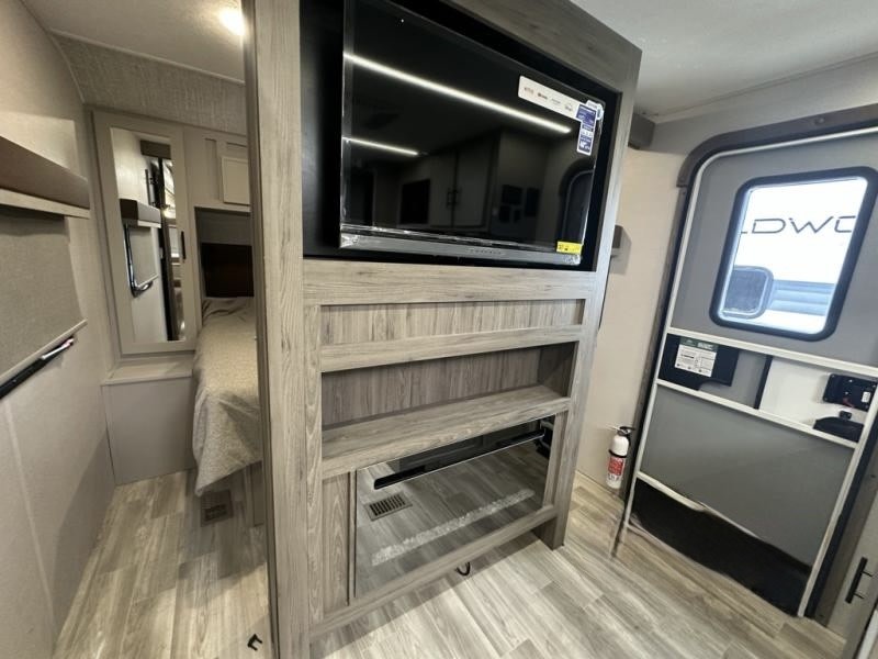 RV rental interior with a TV, storage shelves, and main entry door. A bedroom area is glimpsed to the left.. Forest River Vibe 2025