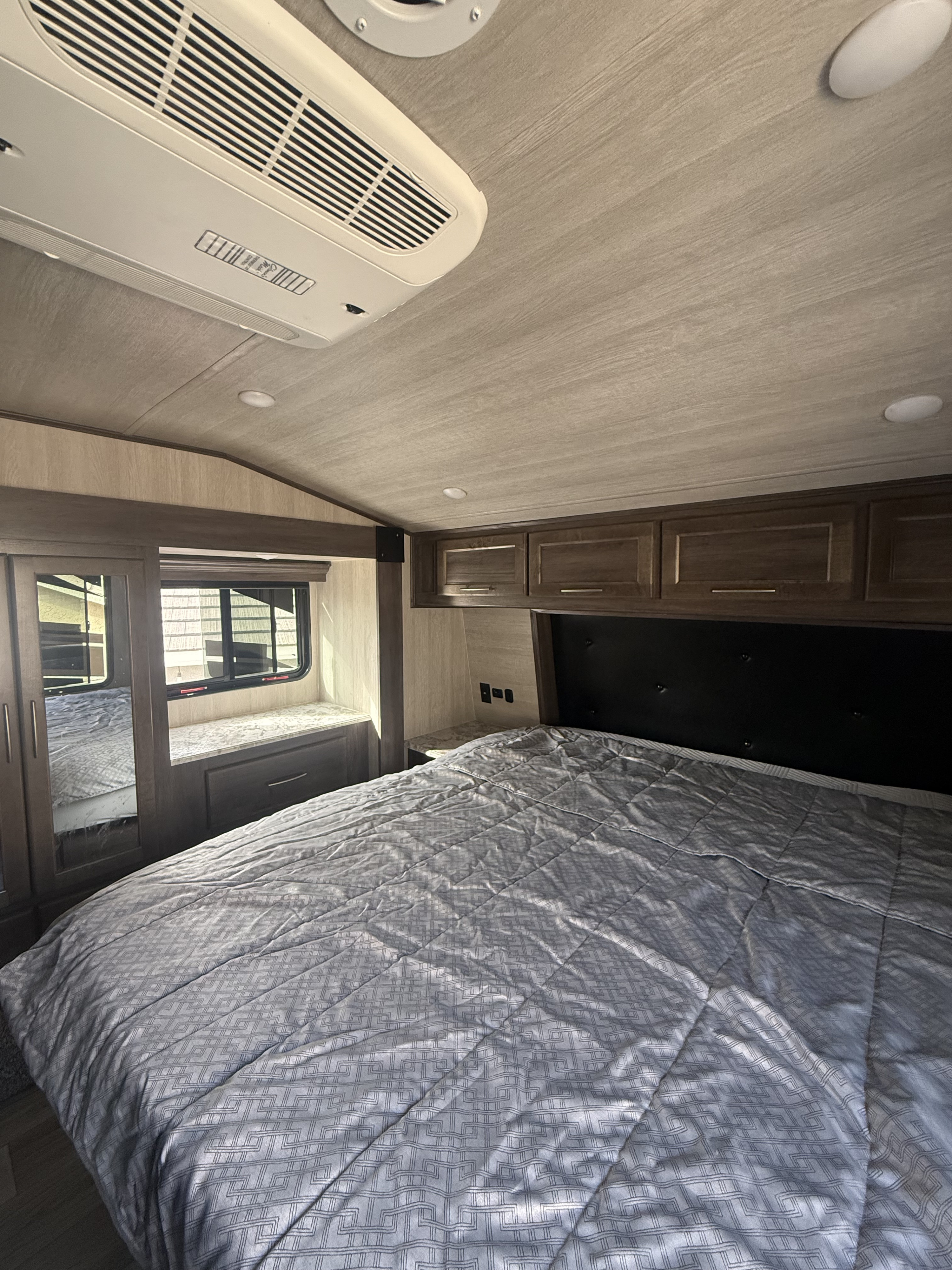 Spacious RV rental bedroom featuring a large bed with patterned bedding, overhead cabinets, AC unit, and window providing natural light.. Genesis Supreme Genesis Supreme Toy Hauler 2025