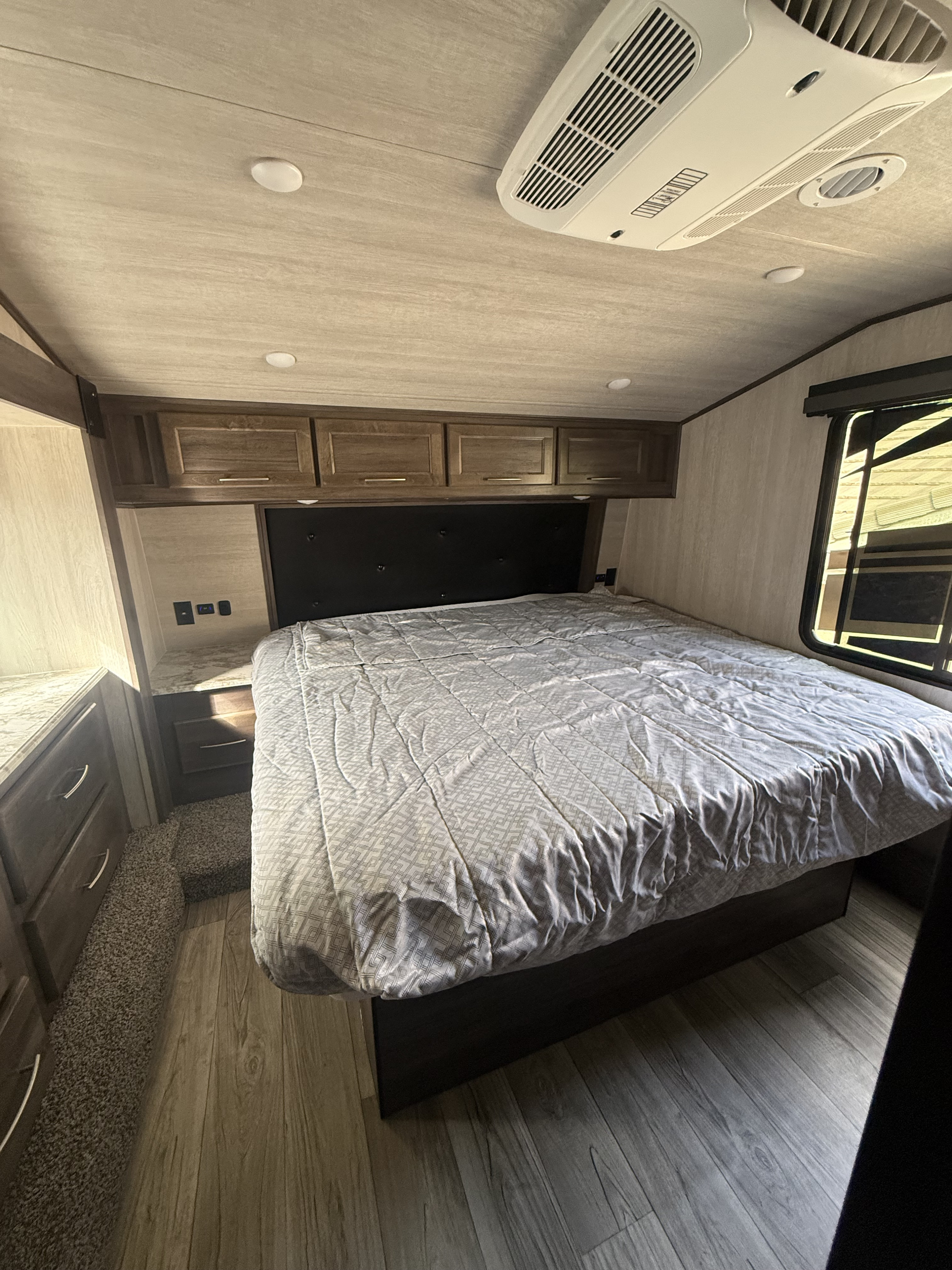 Spacious RV rental bedroom featuring a queen bed, overhead storage, AC, and a bright window. Wood-look flooring and carpet.. Genesis Supreme Genesis Supreme Toy Hauler 2025