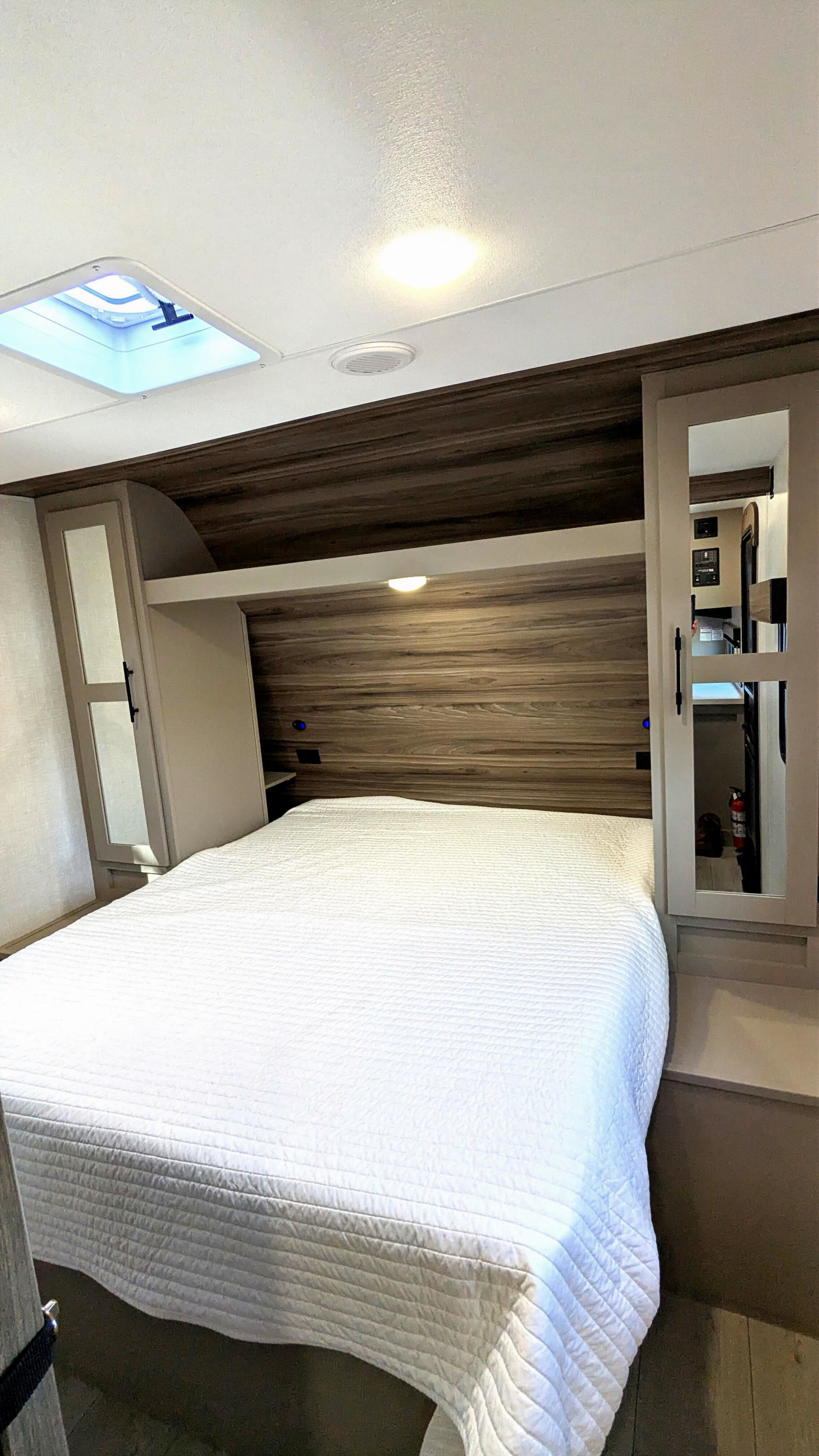 Rv rental bedroom: a comfy white-quilted bed, wooden headboard, overhead cabinets, and a skylight for natural light.. KZ Connect SE 2025