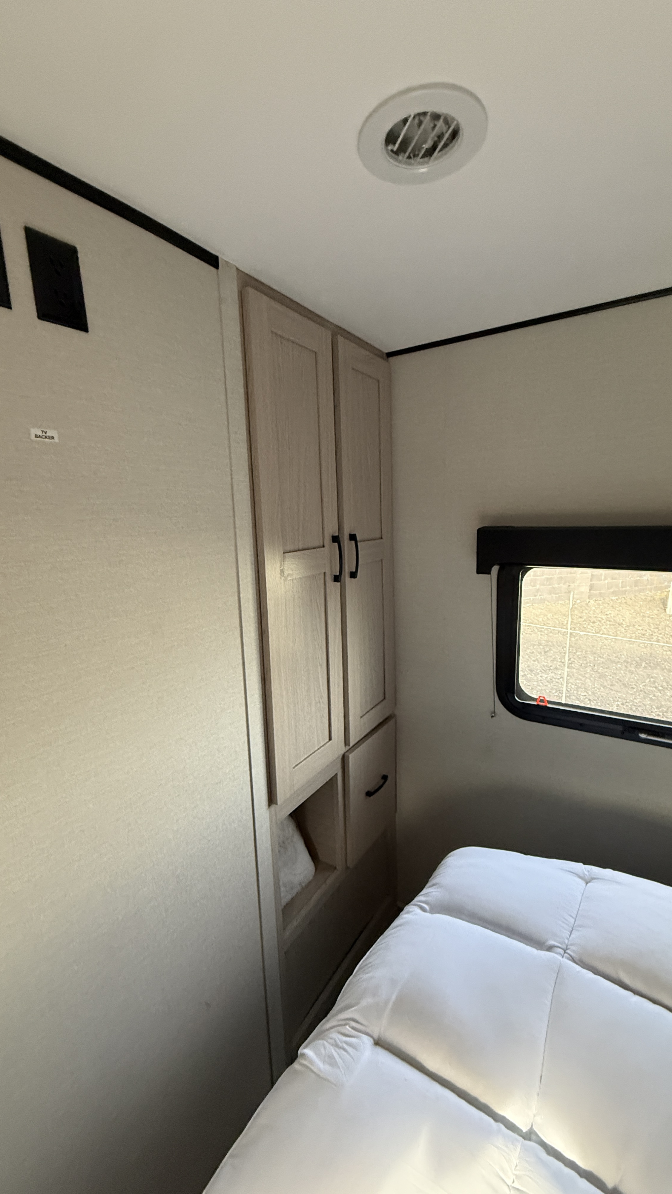 Cozy RV rental bedroom featuring a light wood cabinet, window, white bed, and ceiling vent. TV backer area visible.. Coachmen Apex 293rlds 2022