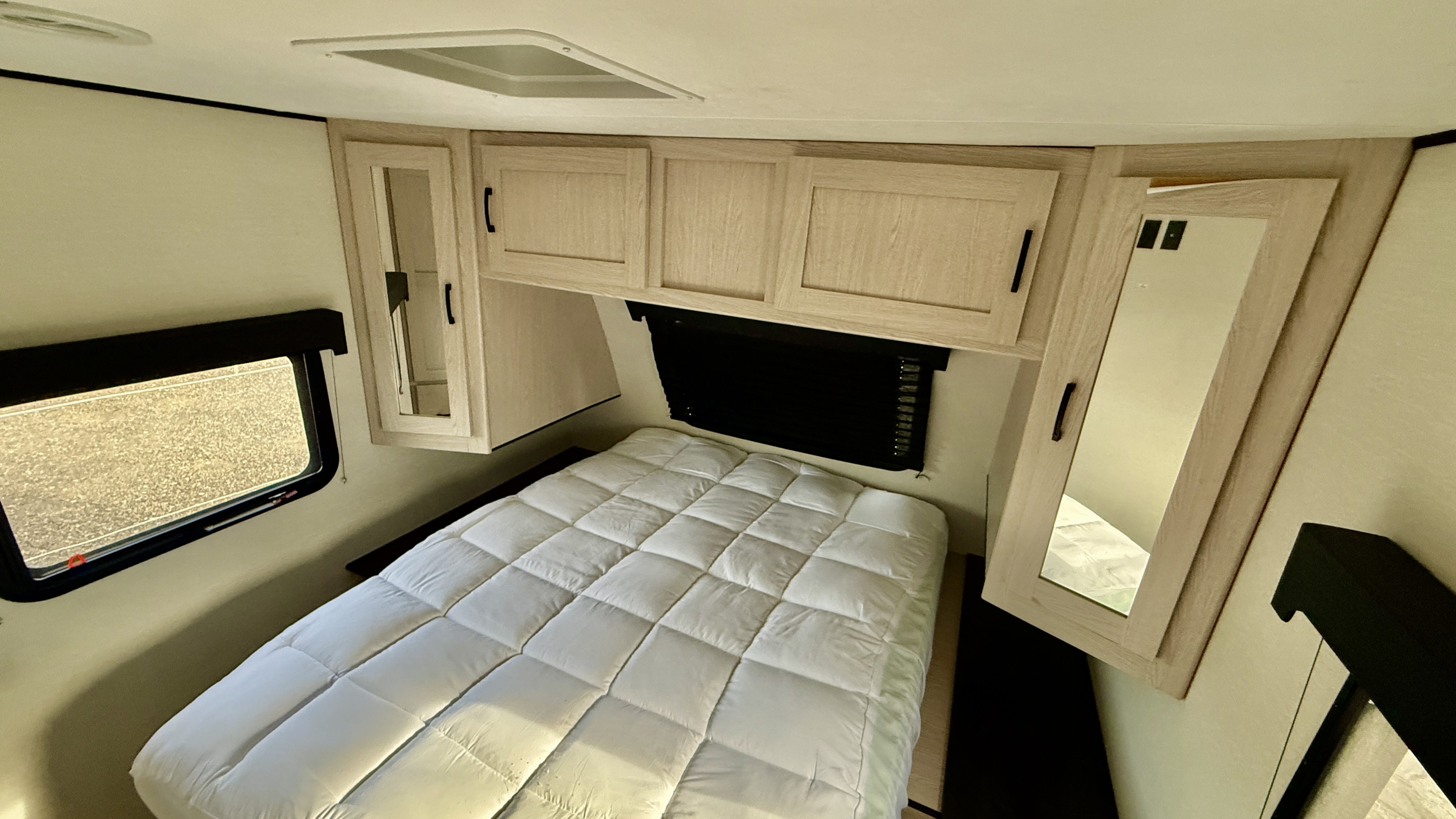 Cozy RV rental bedroom with a white quilted bed, light wood overhead cabinets, and a side window, offering a comfortable space.. Coachmen Apex 293rlds 2022