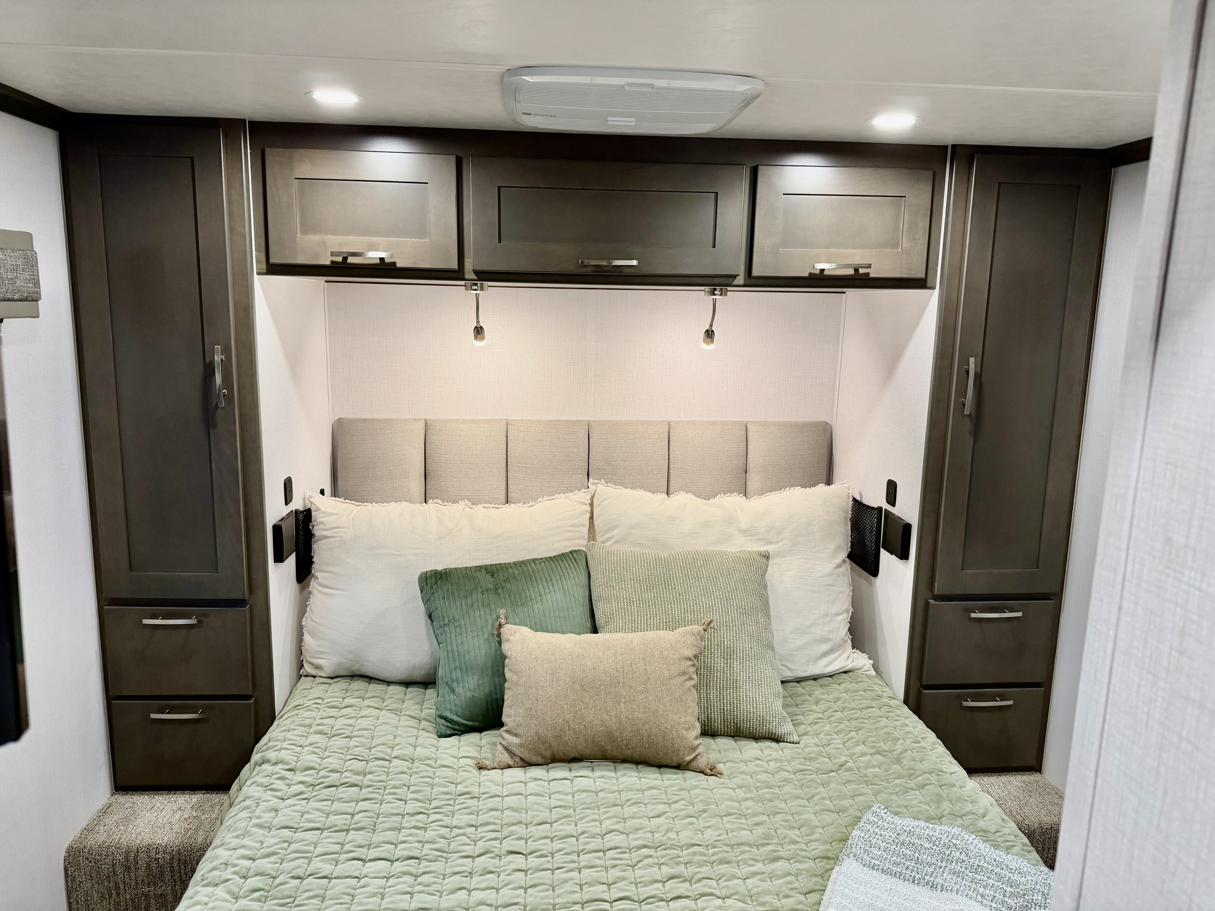 Modern RV rental bedroom showcases a comfortable bed with green accents, dark wood storage, and practical reading lights.. Dynamax Explore ISATA 5 Explorer Extreme Package 2026