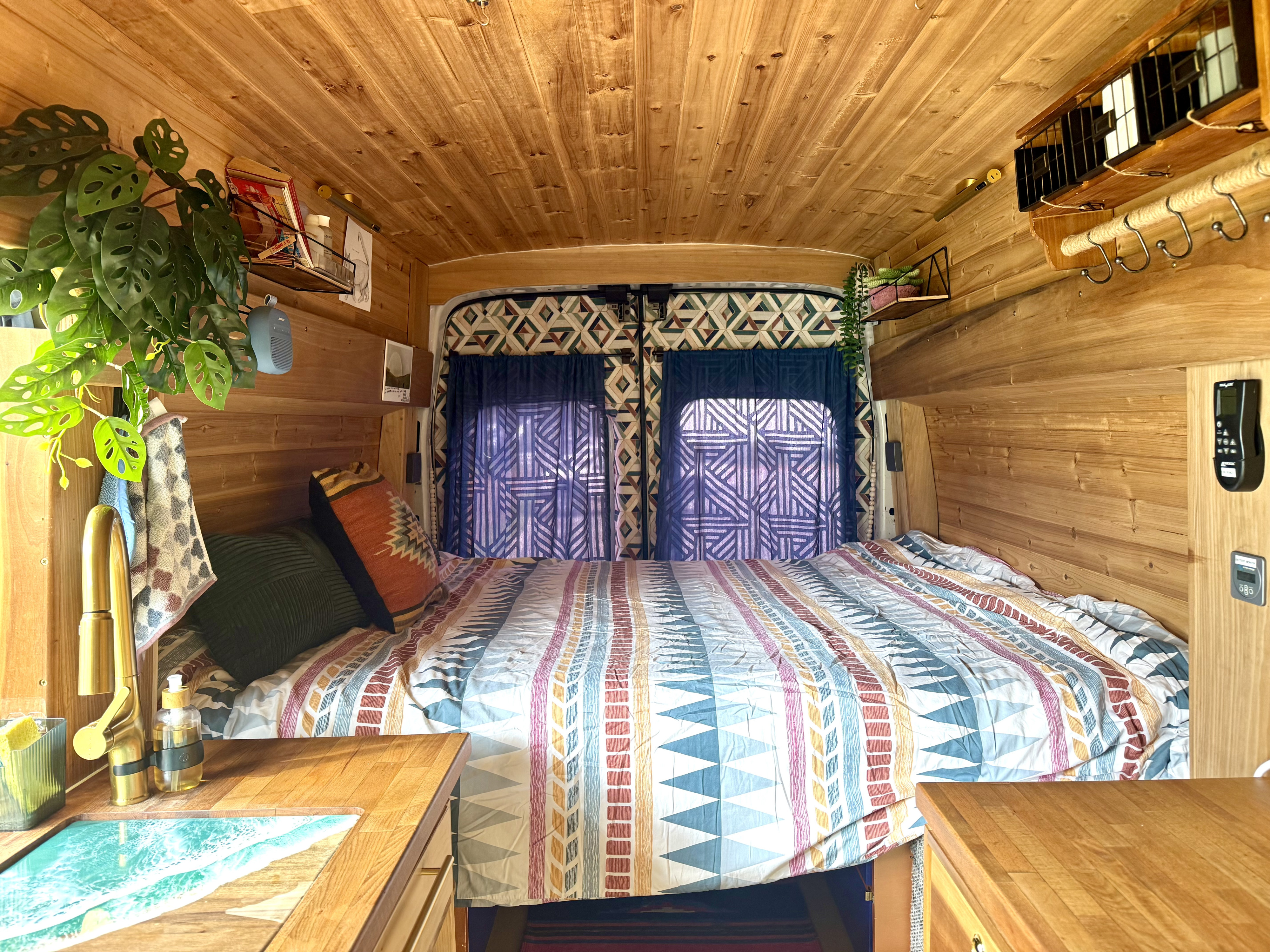 Warm wood-paneled RV rental interior: a cozy bed, unique ocean-themed sink, and vibrant decor for a comfortable journey.. Ford Transit 2019