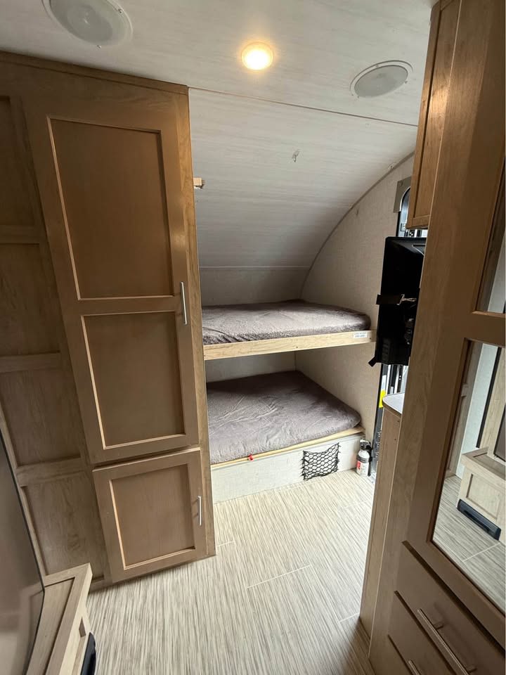 Inside an **rv rental**: two compact bunk beds with gray mattresses, light wood cabinets, and textured flooring. Space-saving design.. Forest River R-Pod RP176 2020
