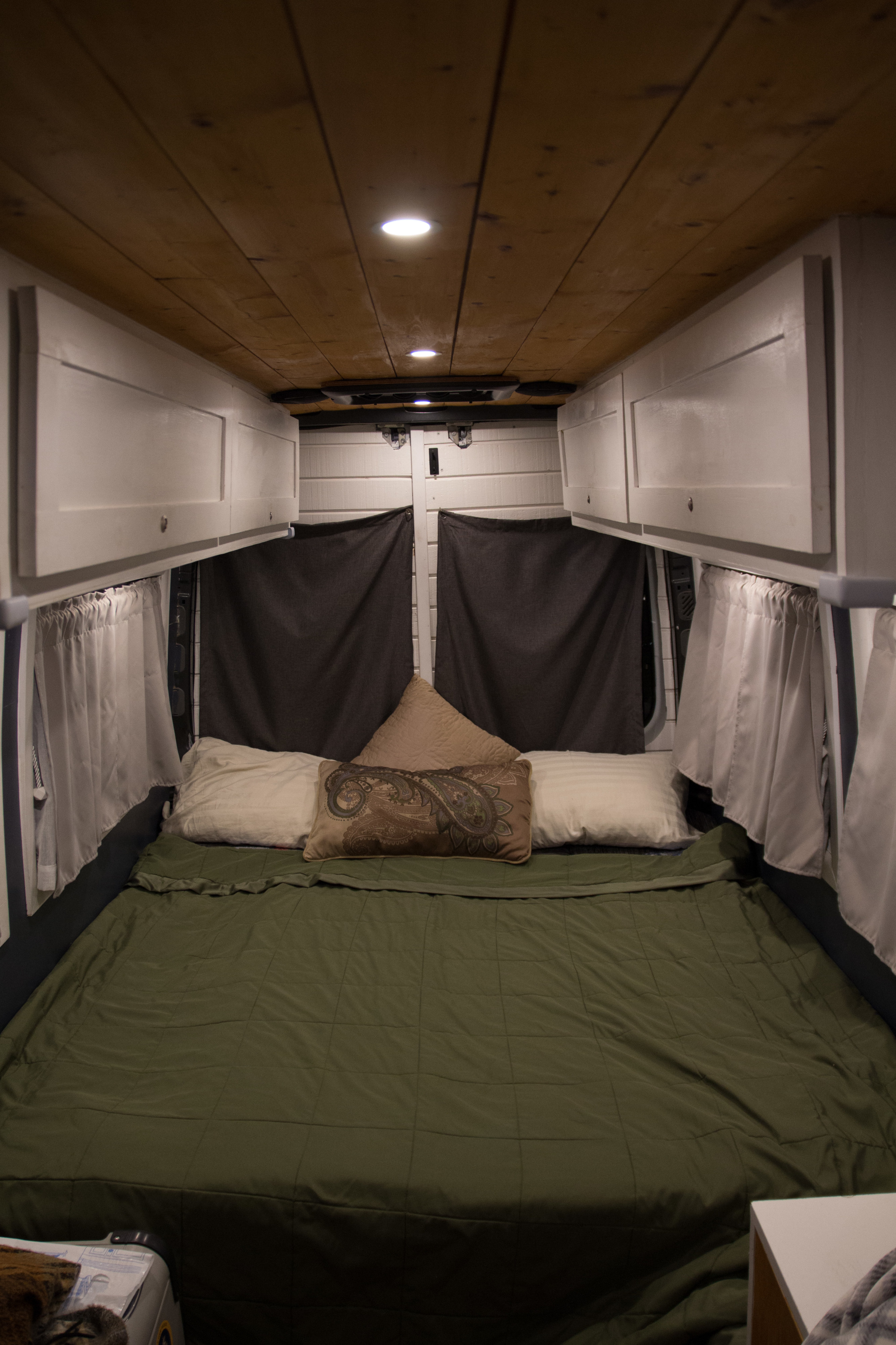 Comfortable RV rental interior featuring a cozy bed, wooden ceiling, custom white cabinets, and blackout curtains.. Mercedes-Benz Sprinter 2014