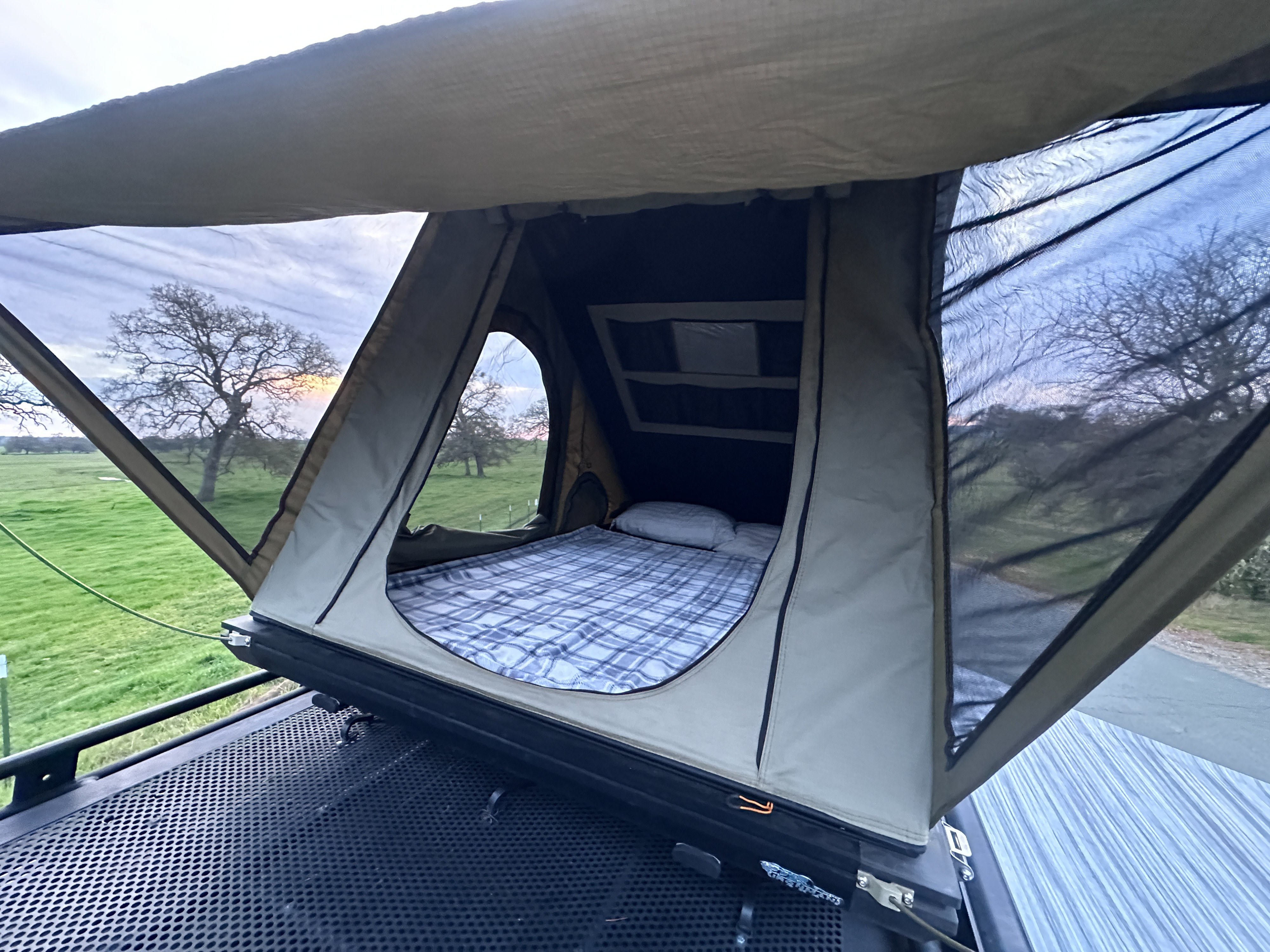 RV rental rooftop tent, ready for cozy nights with a comfy bed and views of lush fields and trees at dusk.. Mercedes-Benz Sprinter 2014