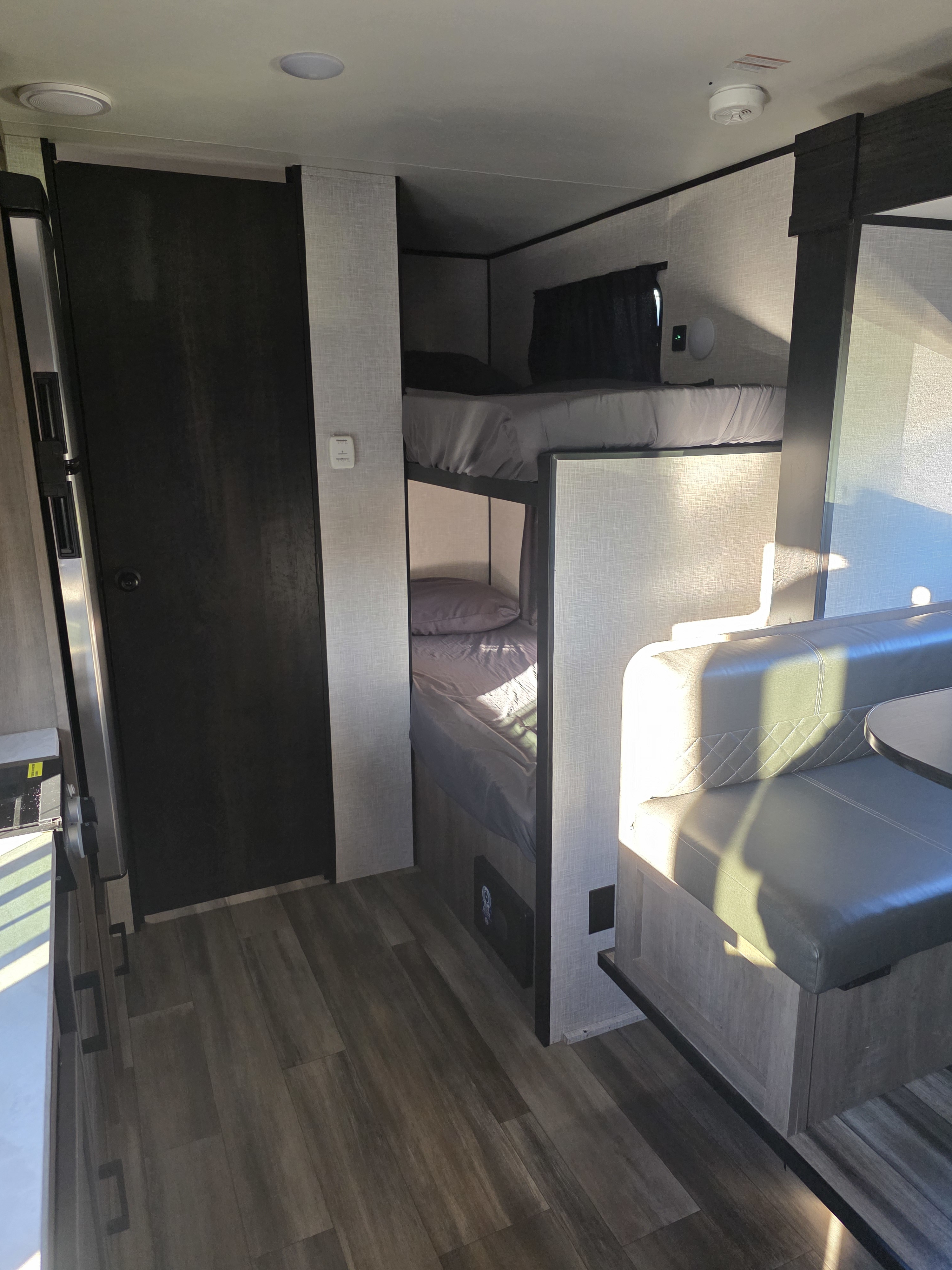 An RV rental interior featuring cozy gray bunk beds, a comfortable dinette with quilted seating, and dark wood-look flooring.. Starcraft Autumn Ridge 2024