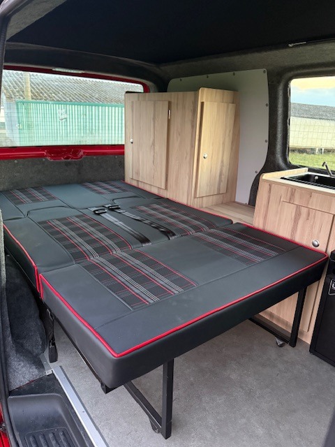 This RV rental features a convertible plaid bed, integrated wooden cabinets, and a compact kitchen for your adventures.. VOLKSWAGEN TRANSPORTER T6 2016