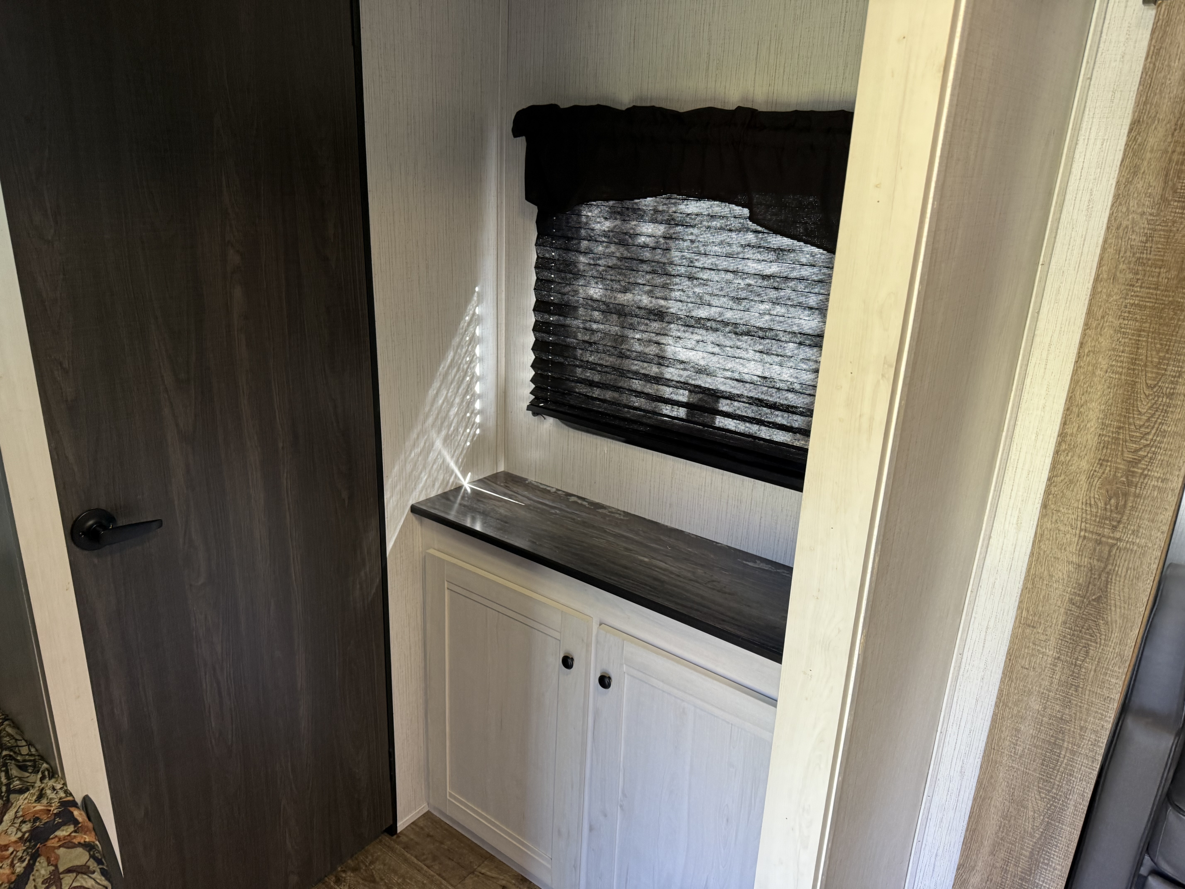 Cozy RV rental interior: Dark wood door, light textured walls, black window blinds, and white cabinets with a dark counter.. Heartland RVs Trail Runner 2022