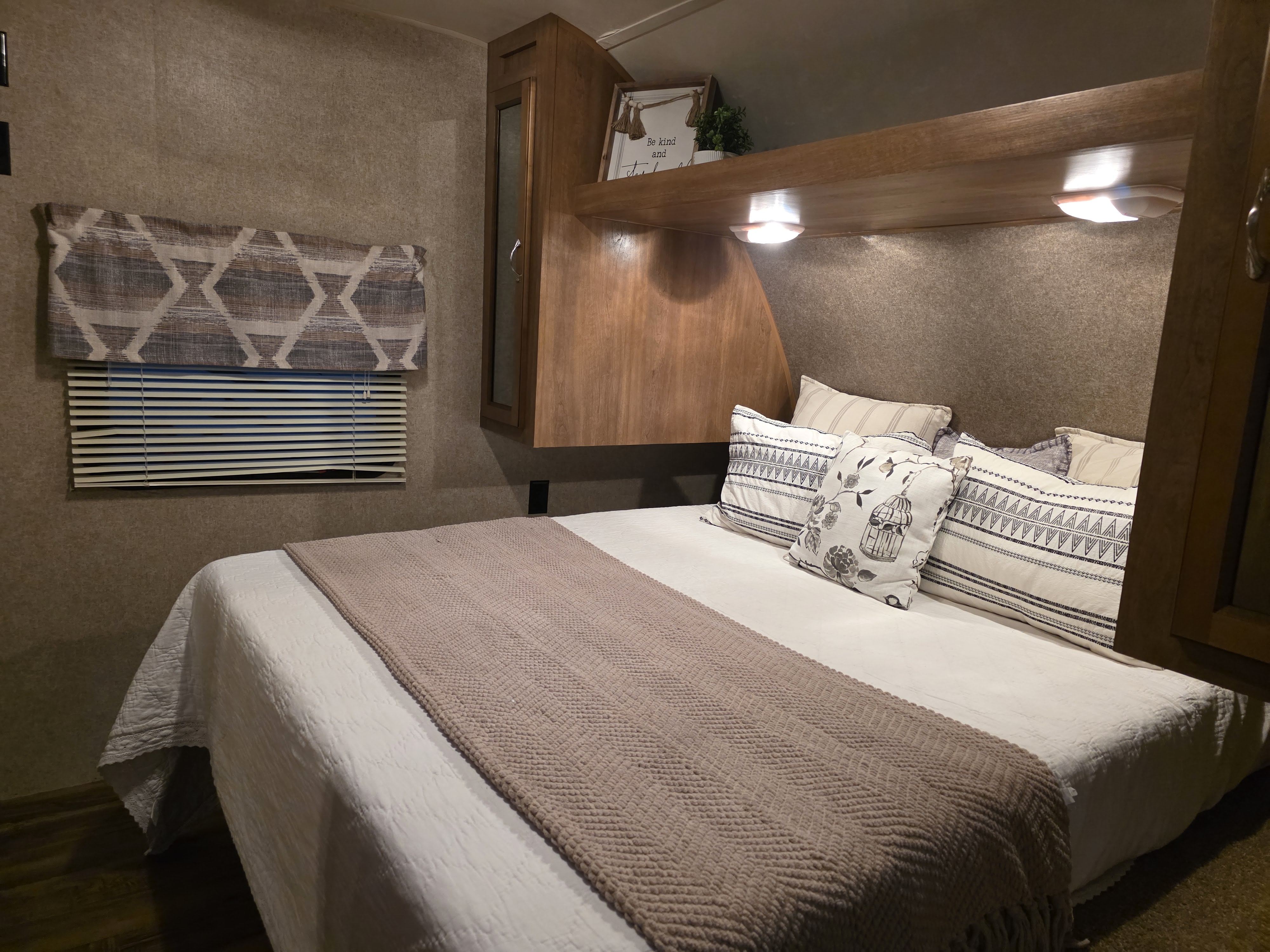 This cozy RV rental bedroom features a comfortable bed with patterned pillows, white bedding, and warm wood accents.. Coachmen Catalina 2016