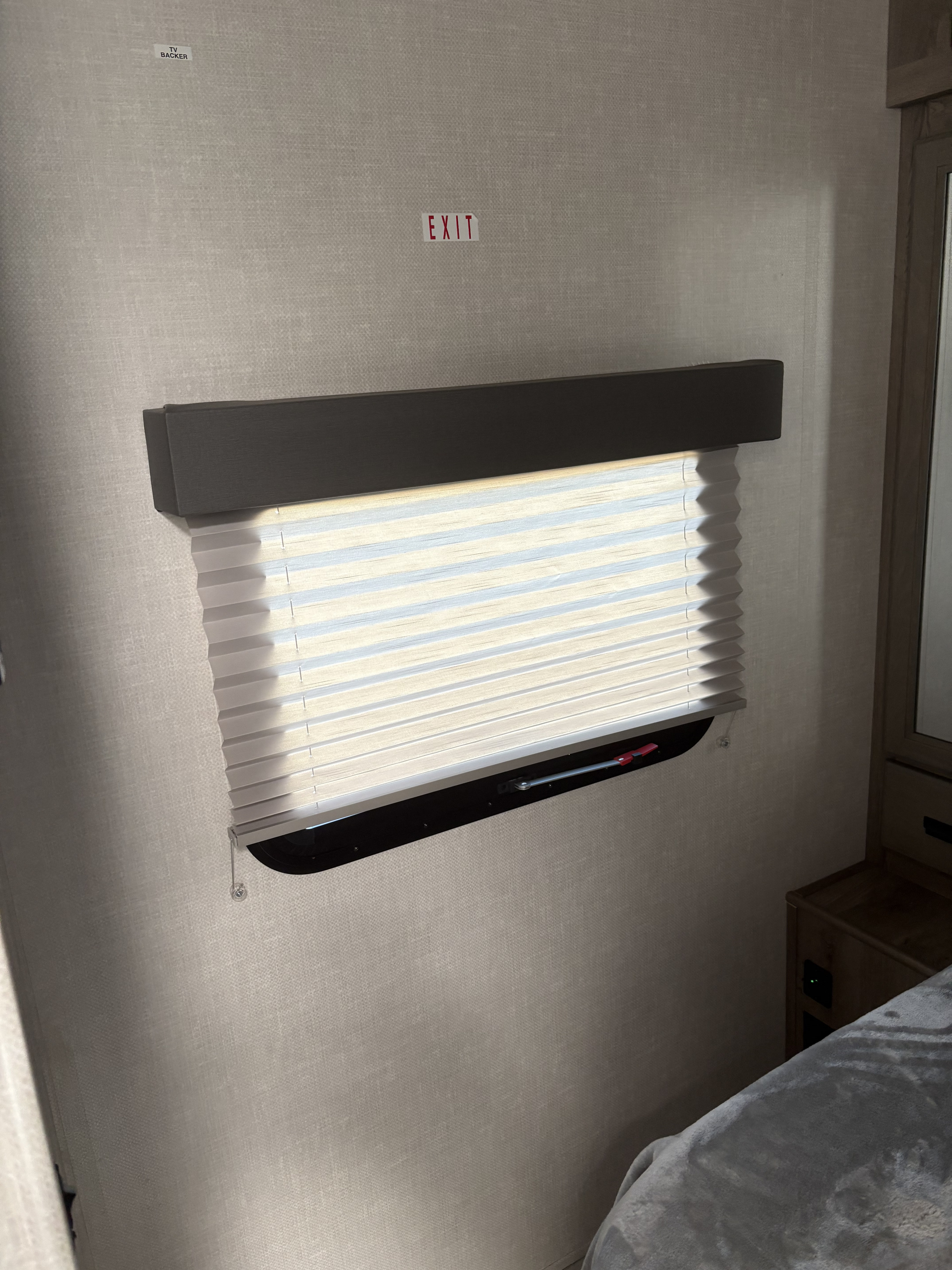 RV rental bedroom: a textured wall with a window and pleated blind, "EXIT" sign, "TV BACKER" label, and bed.. Forest River Surveyor Legend 2022