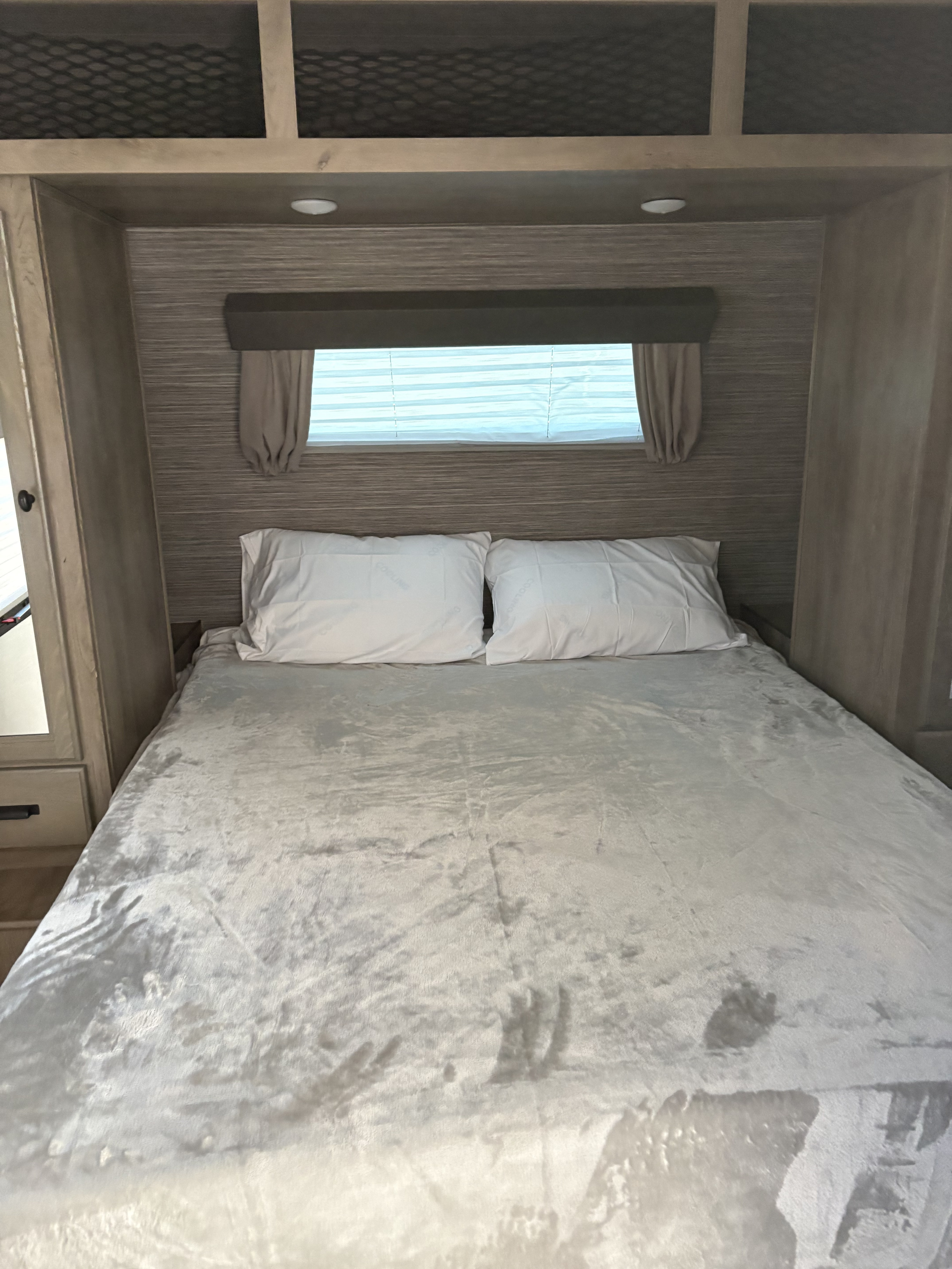 Comfortable RV rental bedroom with a full bed, white pillows, window with blinds, and overhead cabinets for storage.. Forest River Surveyor Legend 2022