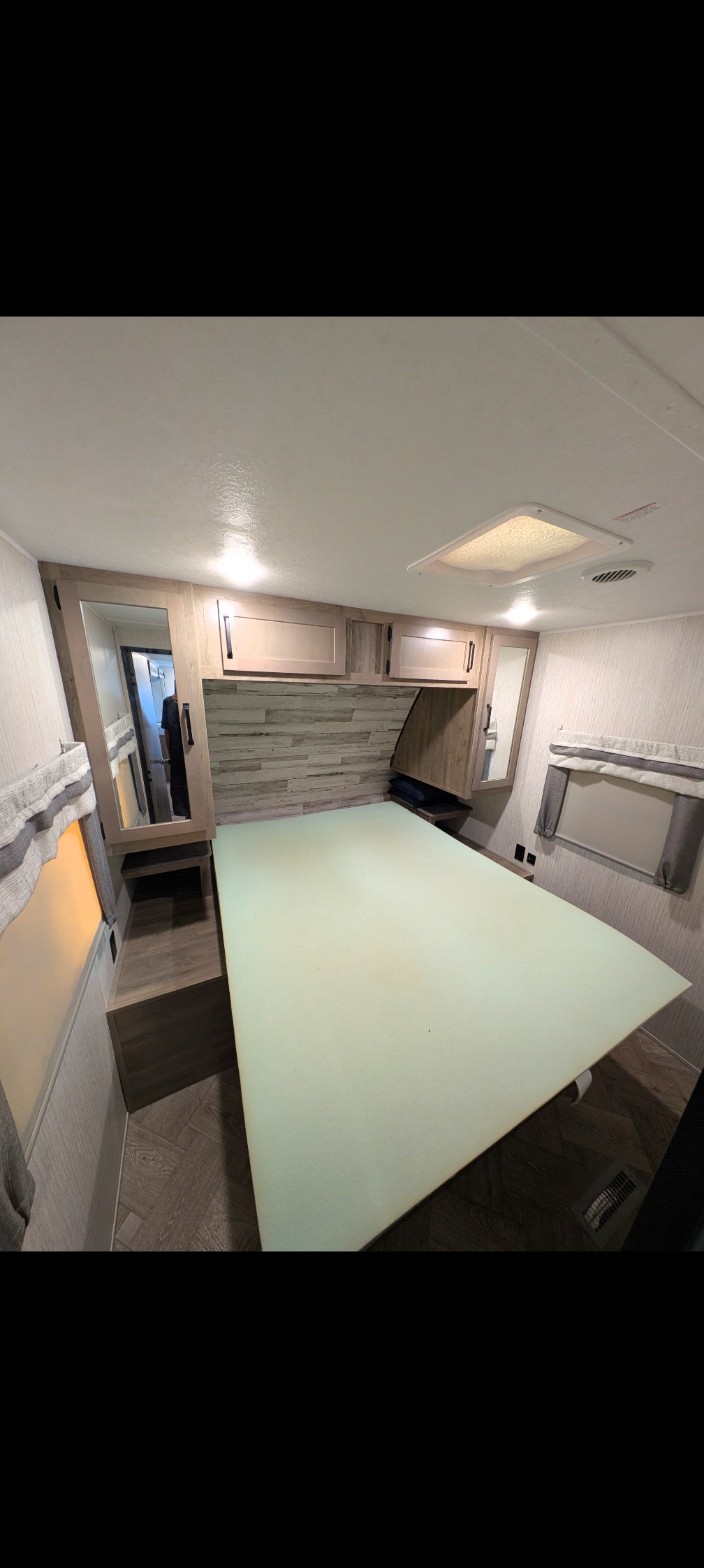 Inside this rv rental bedroom: a light green foam mattress, overhead cabinets, mirror, and window for cozy travel.. Forest River Palomino Puma 2021