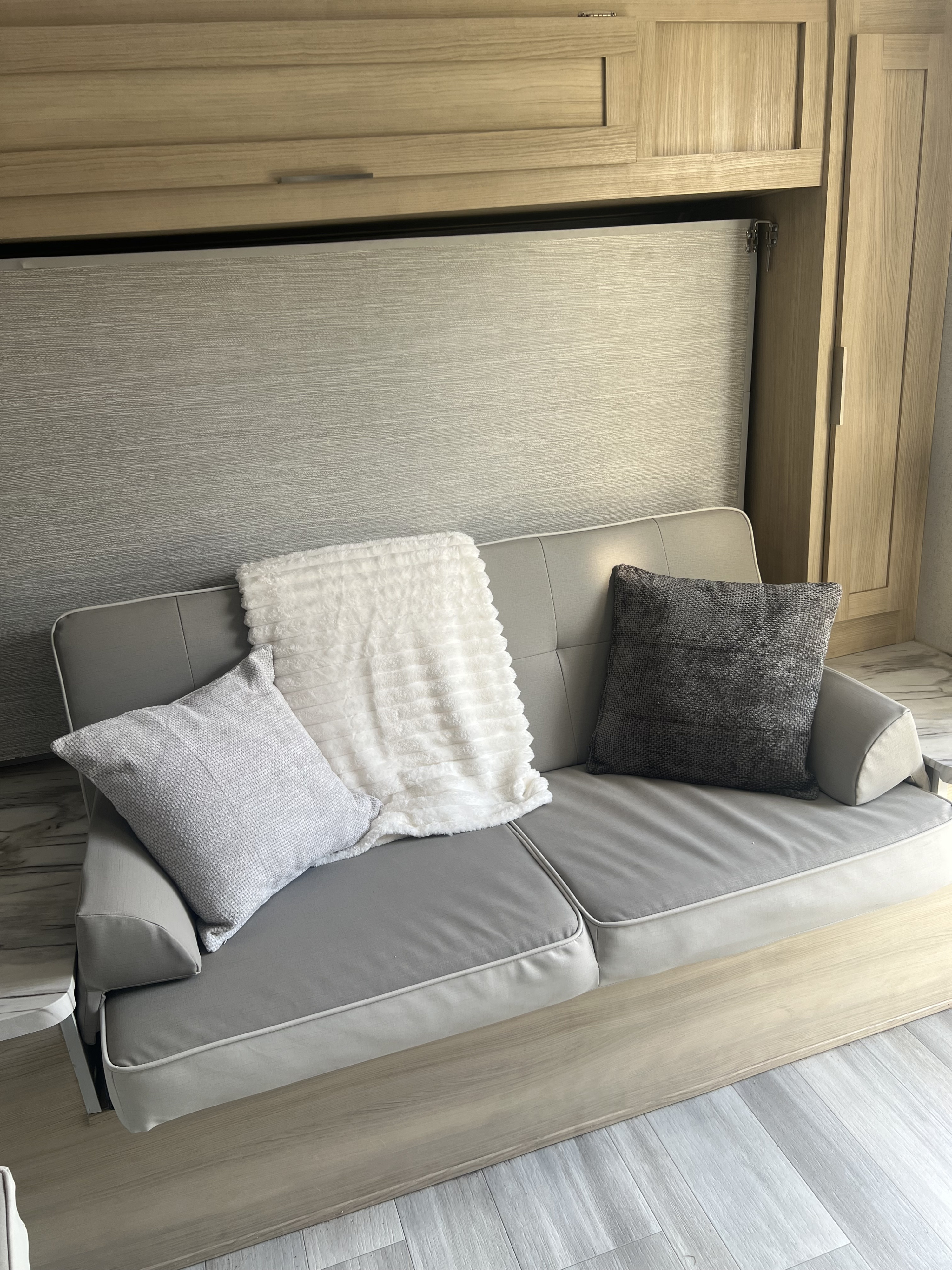 RV rental: Gray couch with decorative pillows & a white blanket. Above are light wood cabinets; below, wood-look flooring.. Forest River Salem FSX 2023